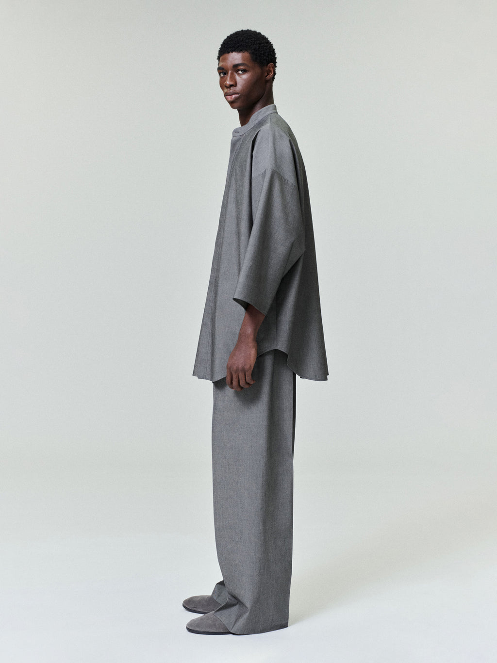 side profile of model wearing relaxed fit grey cotton-wool mandarin collar shirt with cropped sleeves and matching wide-leg trousers