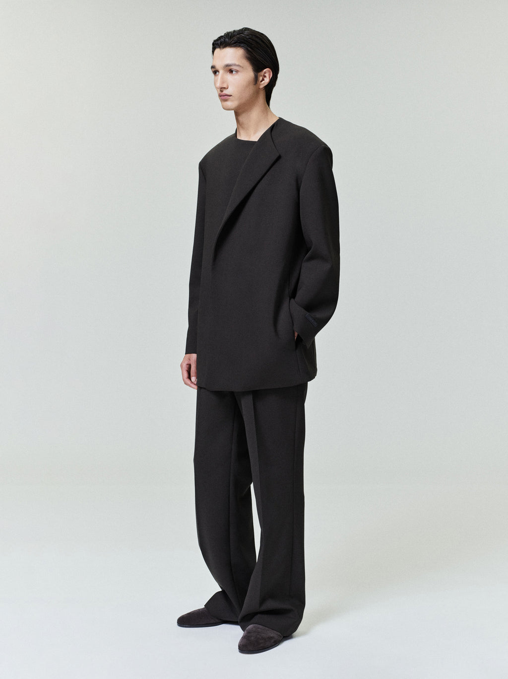 Man wearing oversized black blazer and matching wide-leg trousers standing against light gray background