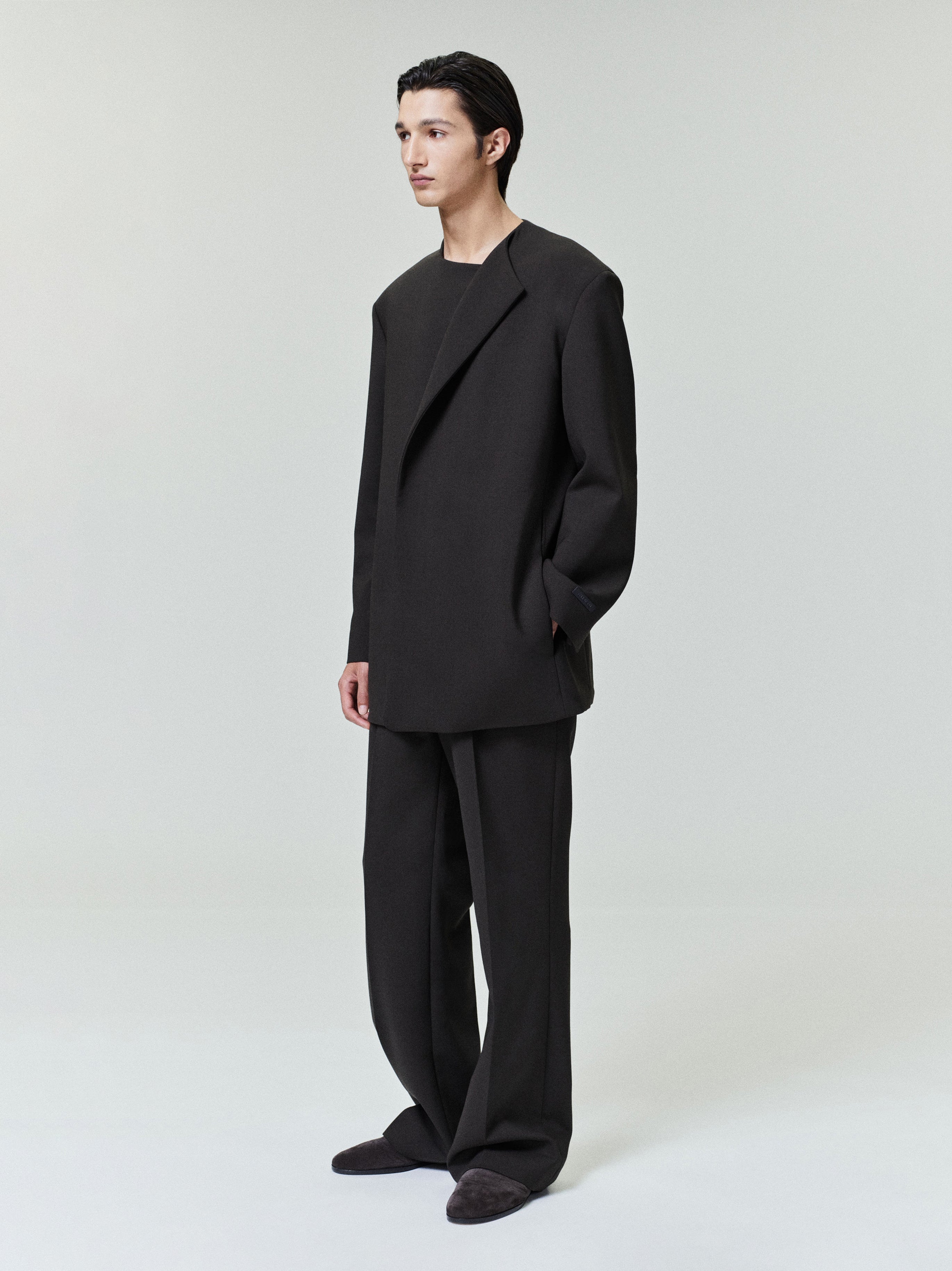 Man wearing oversized black blazer and matching wide-leg trousers standing against light gray background
