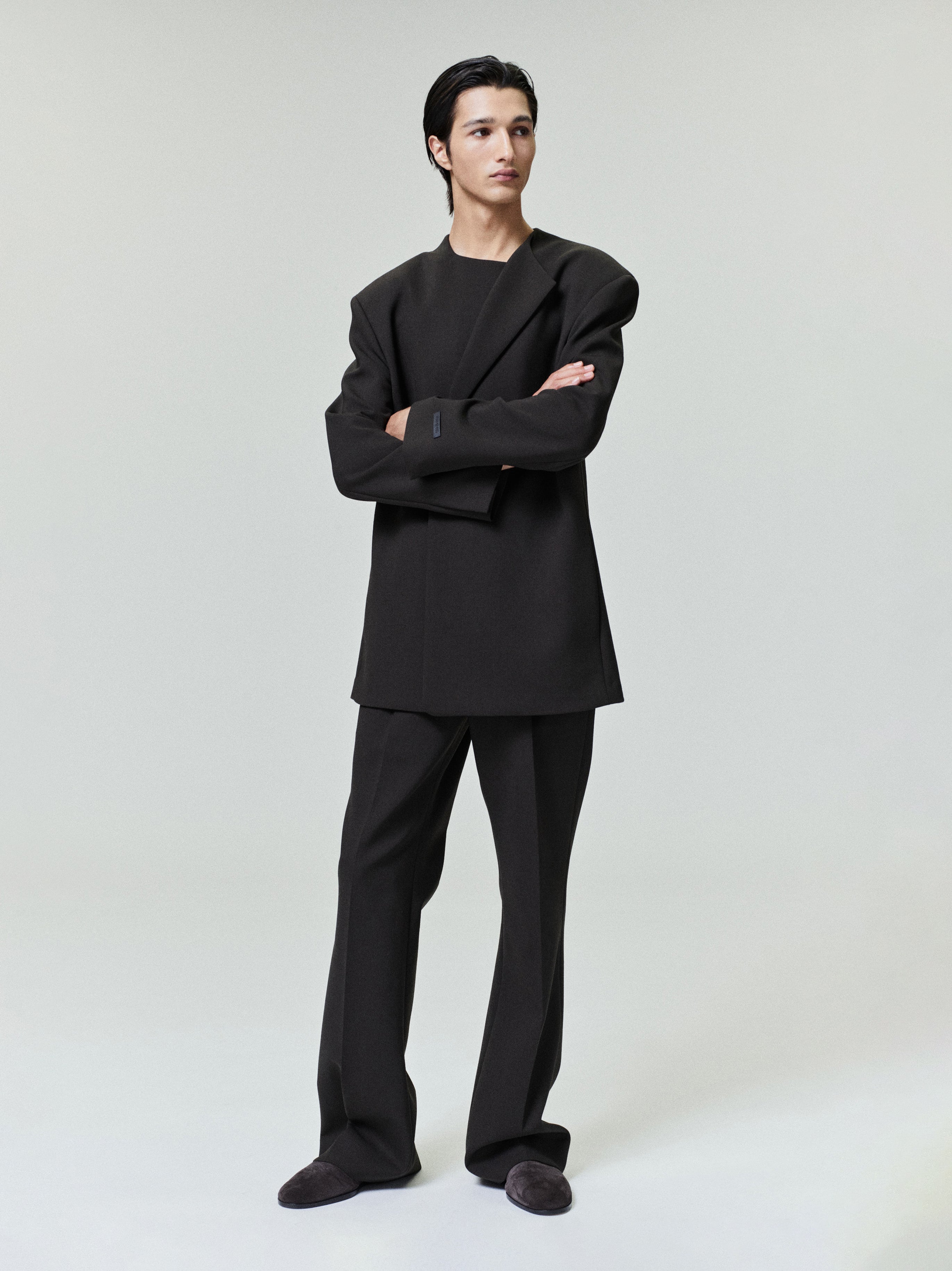 Young man wearing oversized black blazer and matching trousers standing against plain light gray background