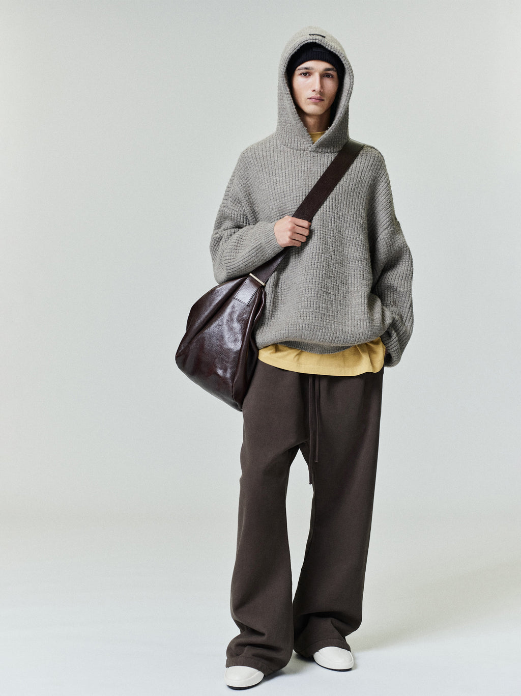 Model wearing dark brown Heavy Fleece Flare Sweatpant paired with oversized gray knit hoodie and dark leather shoulder bag, gallery 0