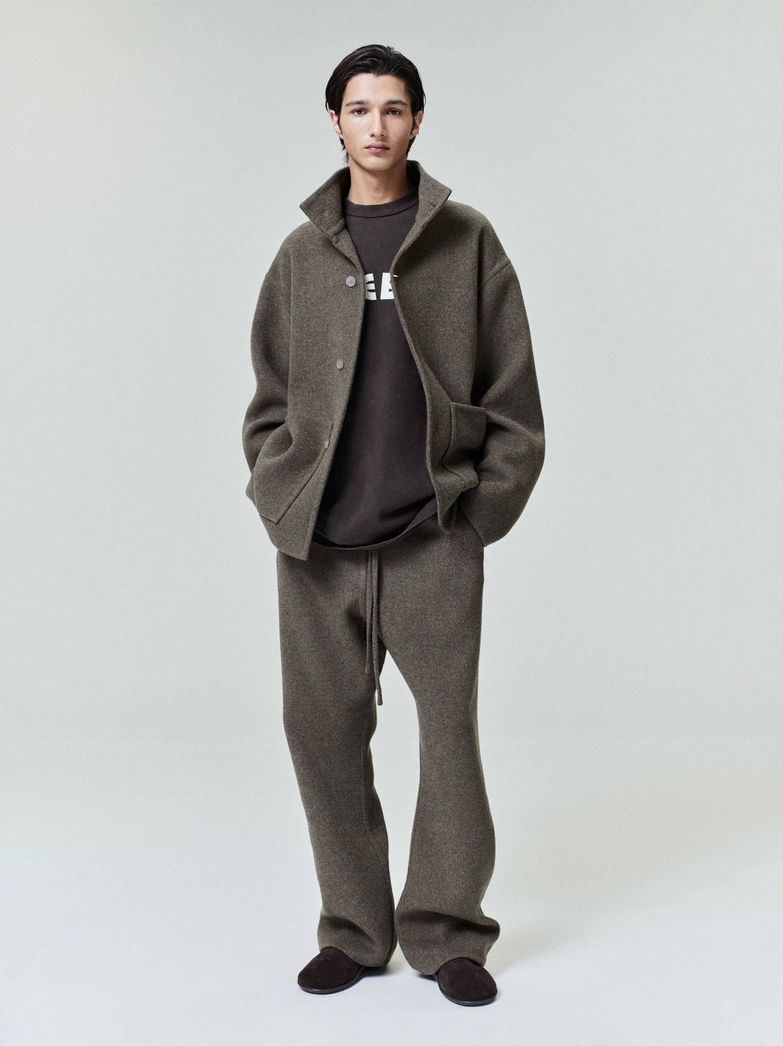 Man wearing a relaxed-fit olive-green wool jacket and matching wide trousers over a dark graphic sweatshirt