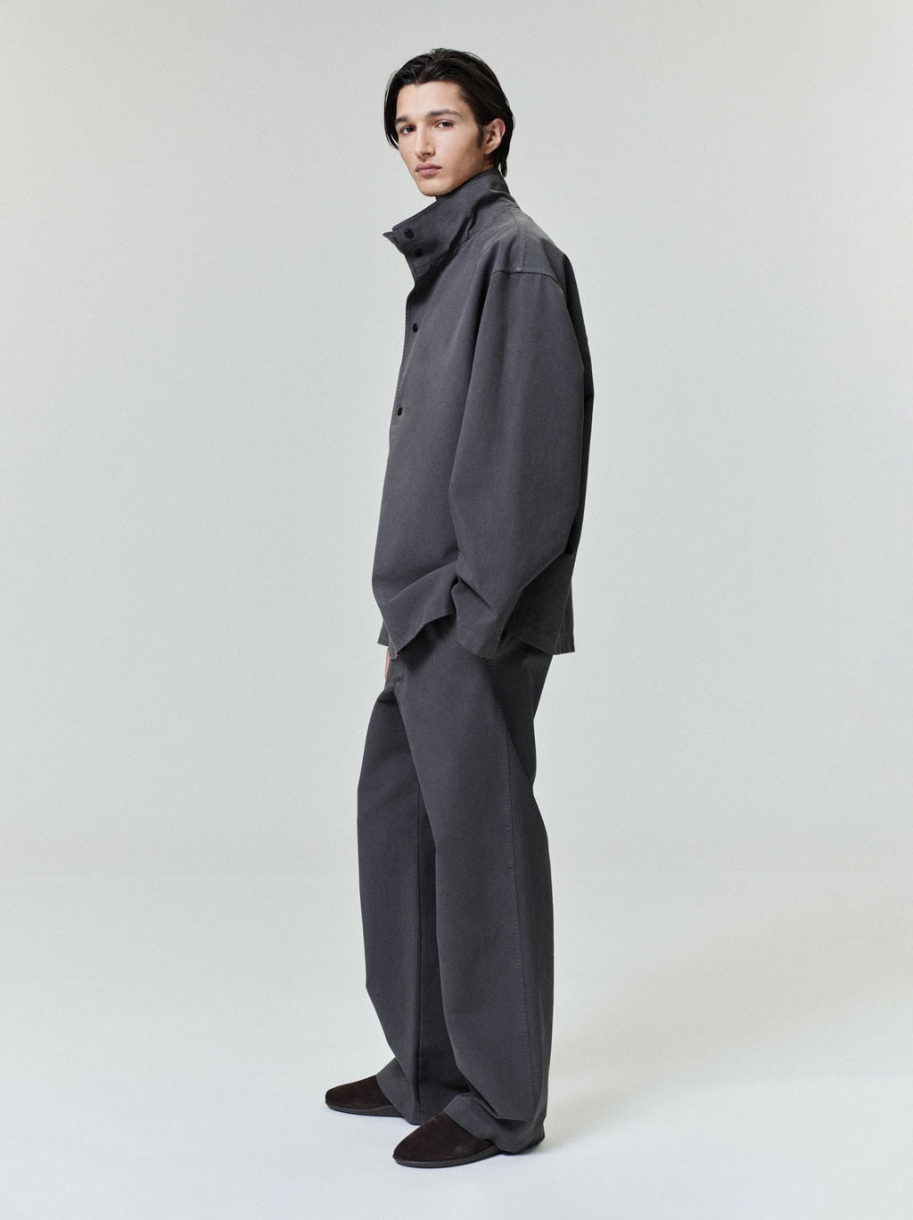 side view of model wearing charcoal garment dyed cotton sport jacket with stand-up collar and wide-legged pants