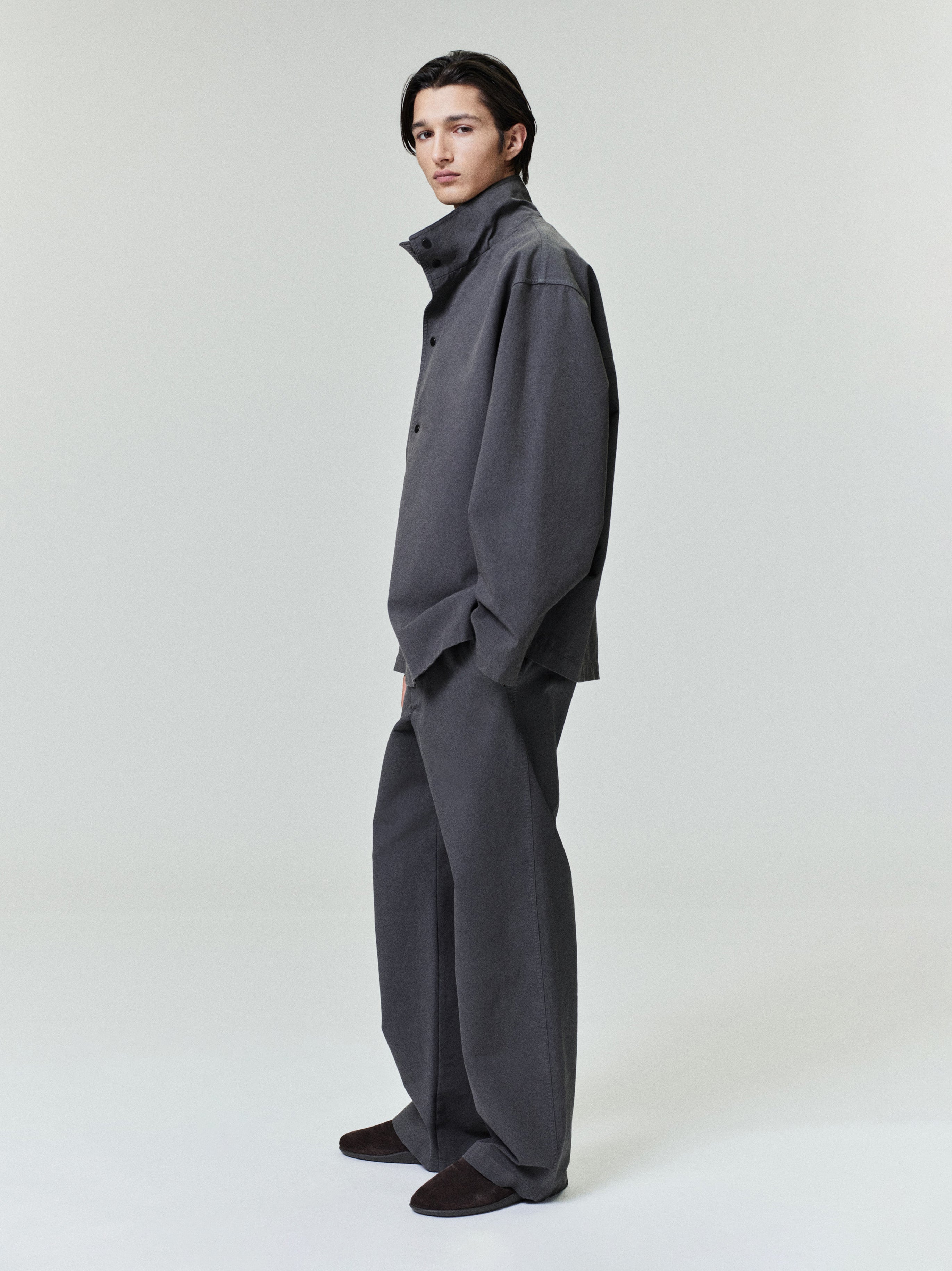 side view of model wearing charcoal garment dyed cotton sport jacket with stand-up collar and wide-legged pants