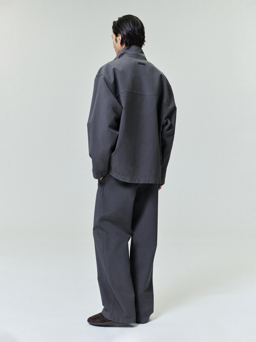 rear view of model wearing loose fit garment dyed cotton sport jacket with large stand collar and matching wide pants