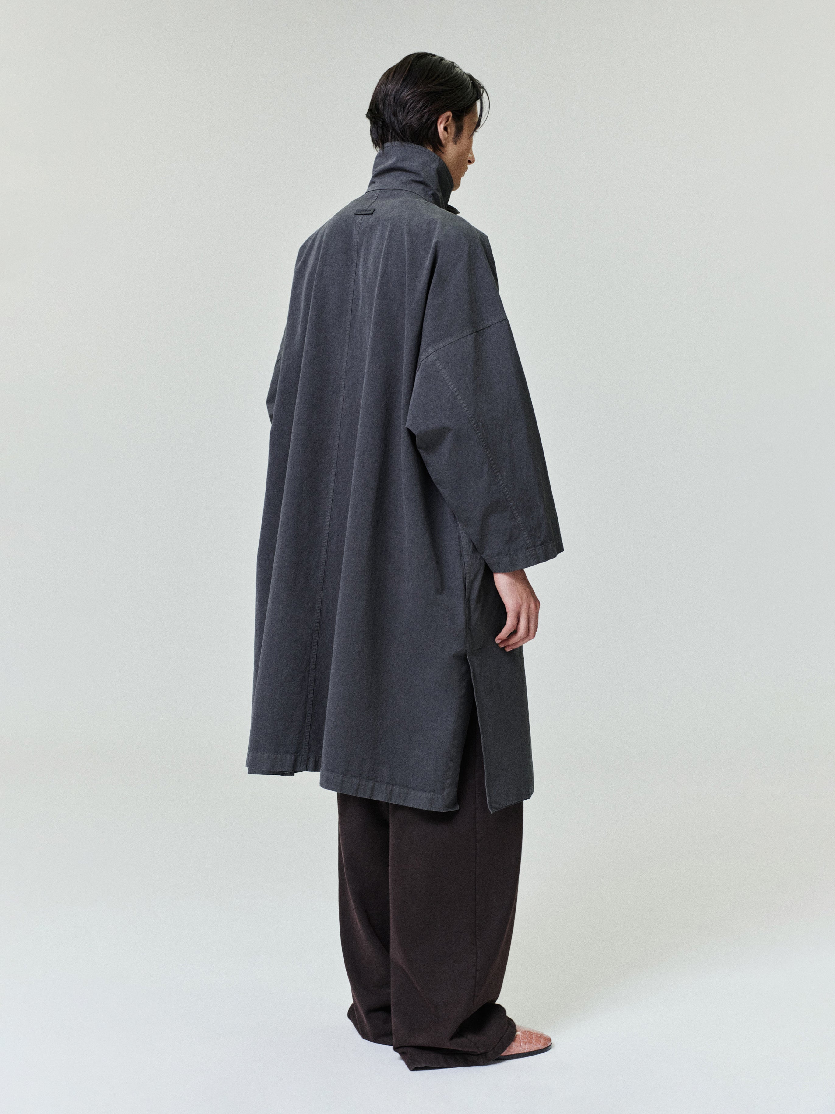 Person wearing a loose dark gray high-collar long coat with wide sleeves and side slits over black wide-leg pants