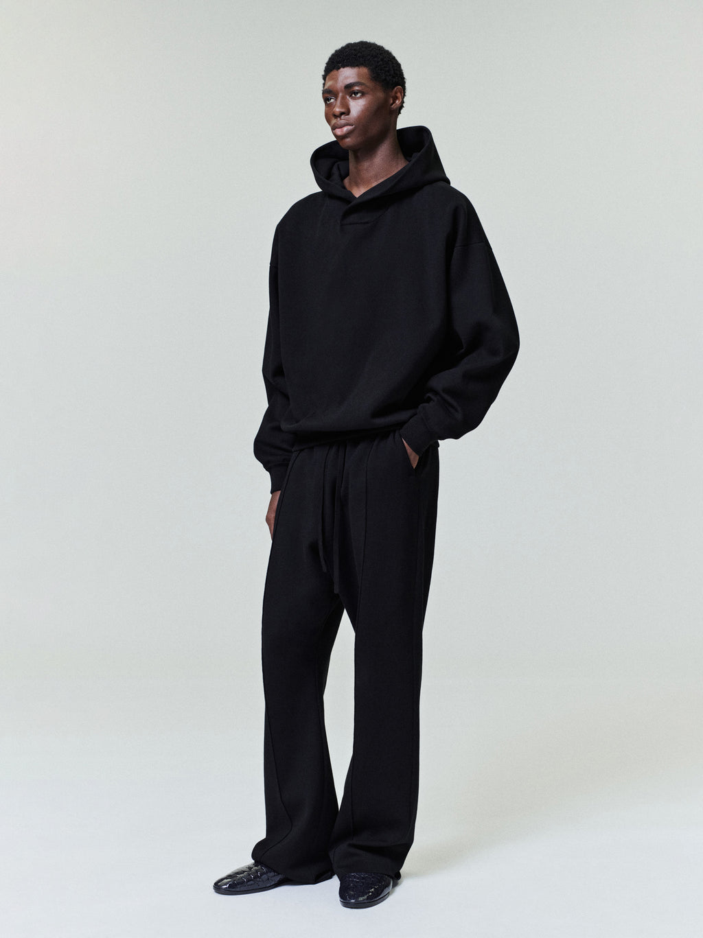 male model wearing relaxed fit black double knit hoodie and matching trousers with ribbed cuffs and hem
