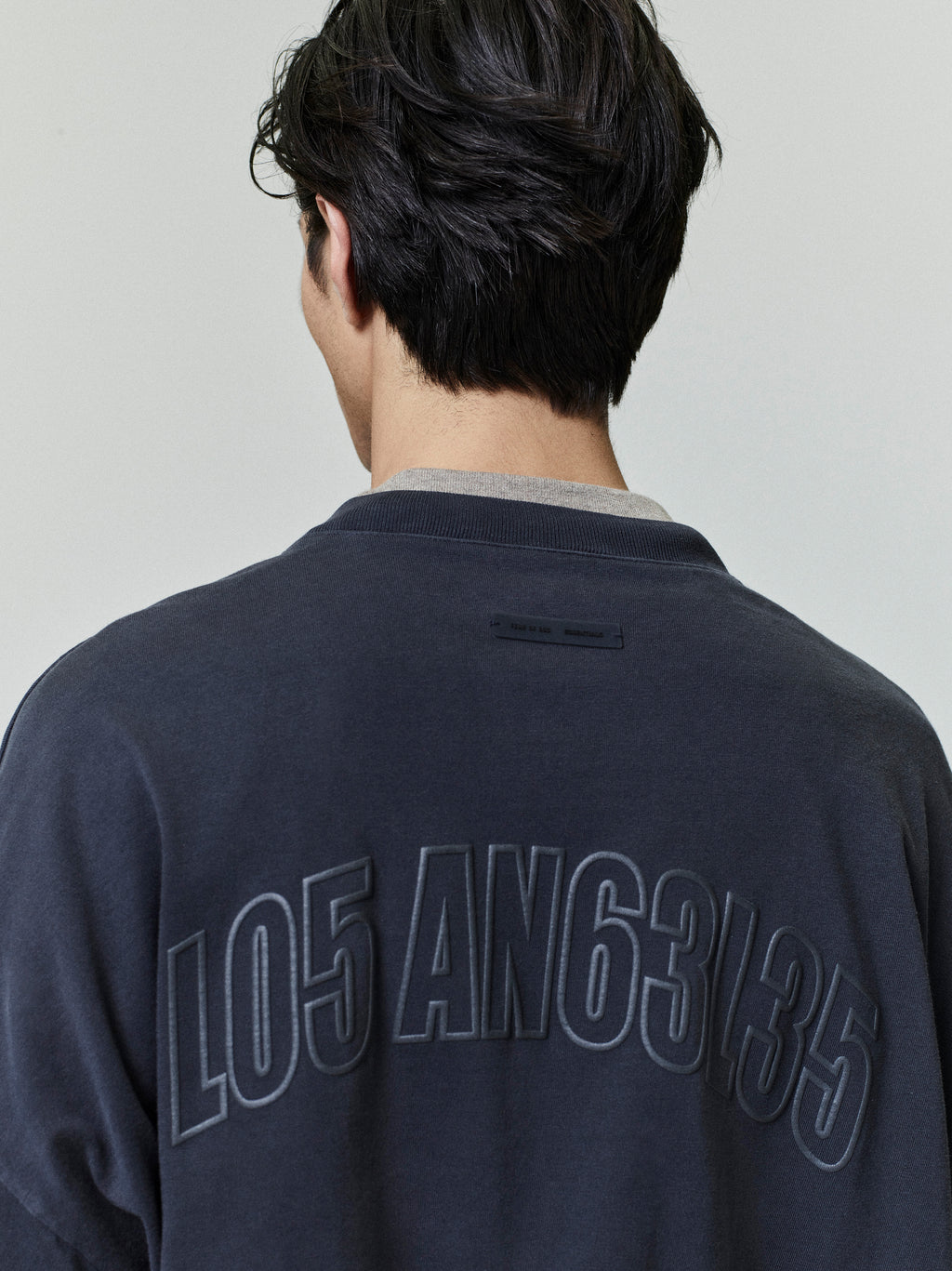 Rear view of man wearing dark Los Angeles 90s Tee with large embossed numeric lettering on back neckline