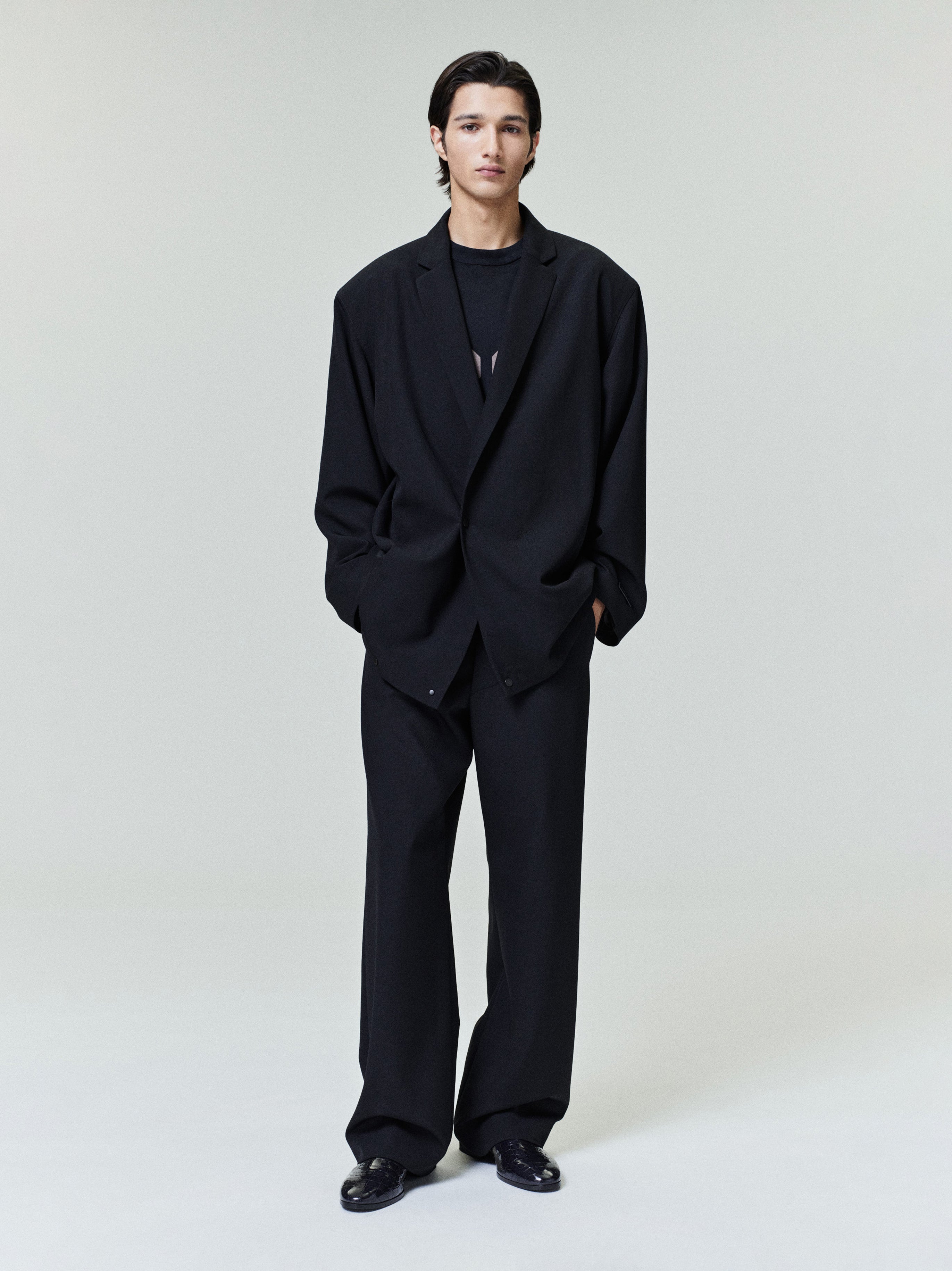 Man standing wearing an oversized black blazer with matching wide black trousers and black shoes