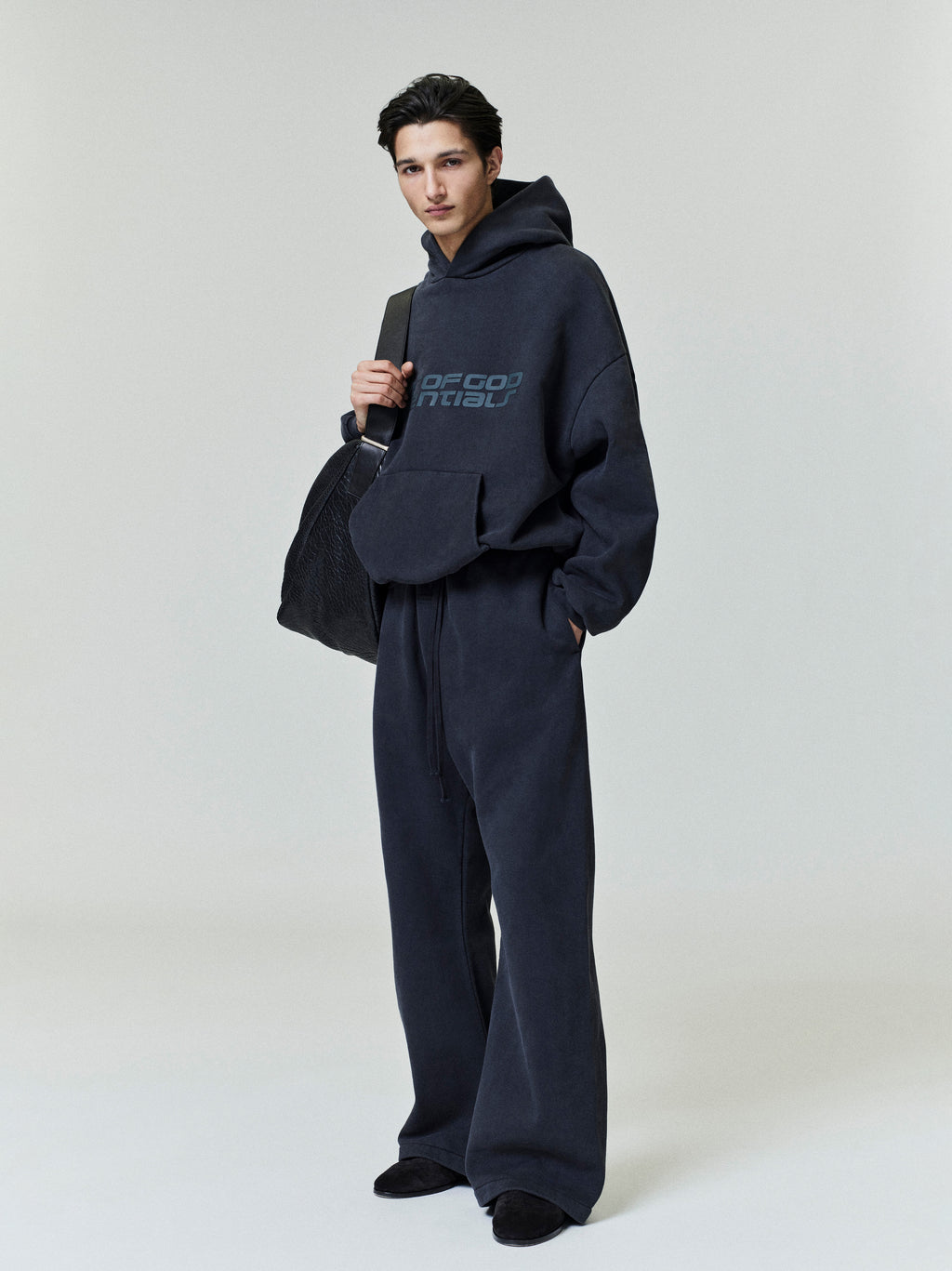 Full-length shot of model wearing dark navy Heavy Fleece 90s Hoodie with matching wide-leg pants and carrying large black bag gallery 0