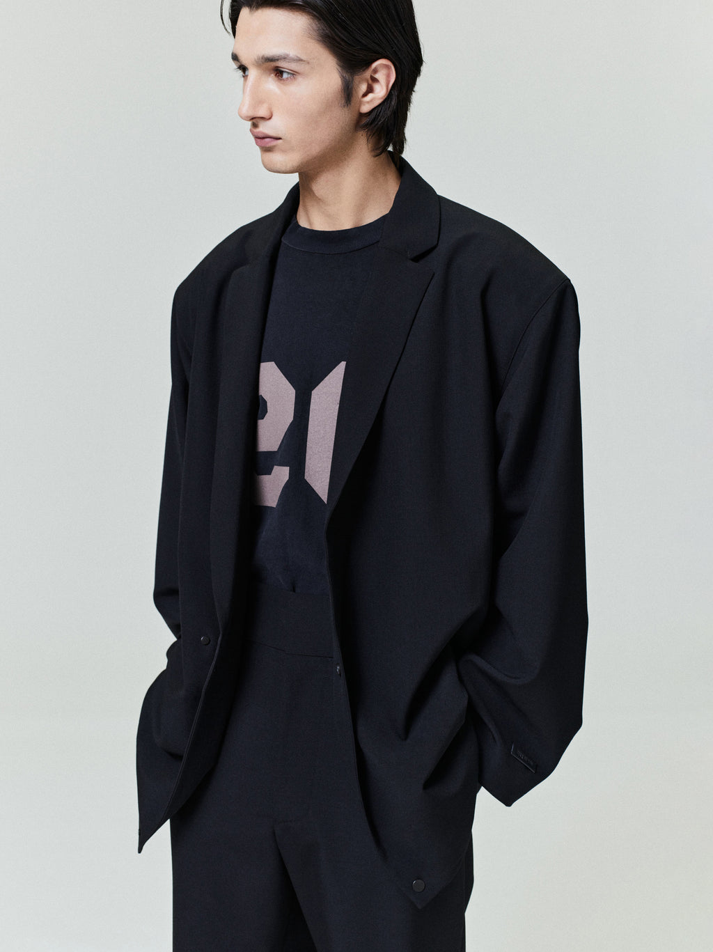 Young man wearing a loose black blazer over a graphic black t-shirt with matching black trousers, hands in pockets