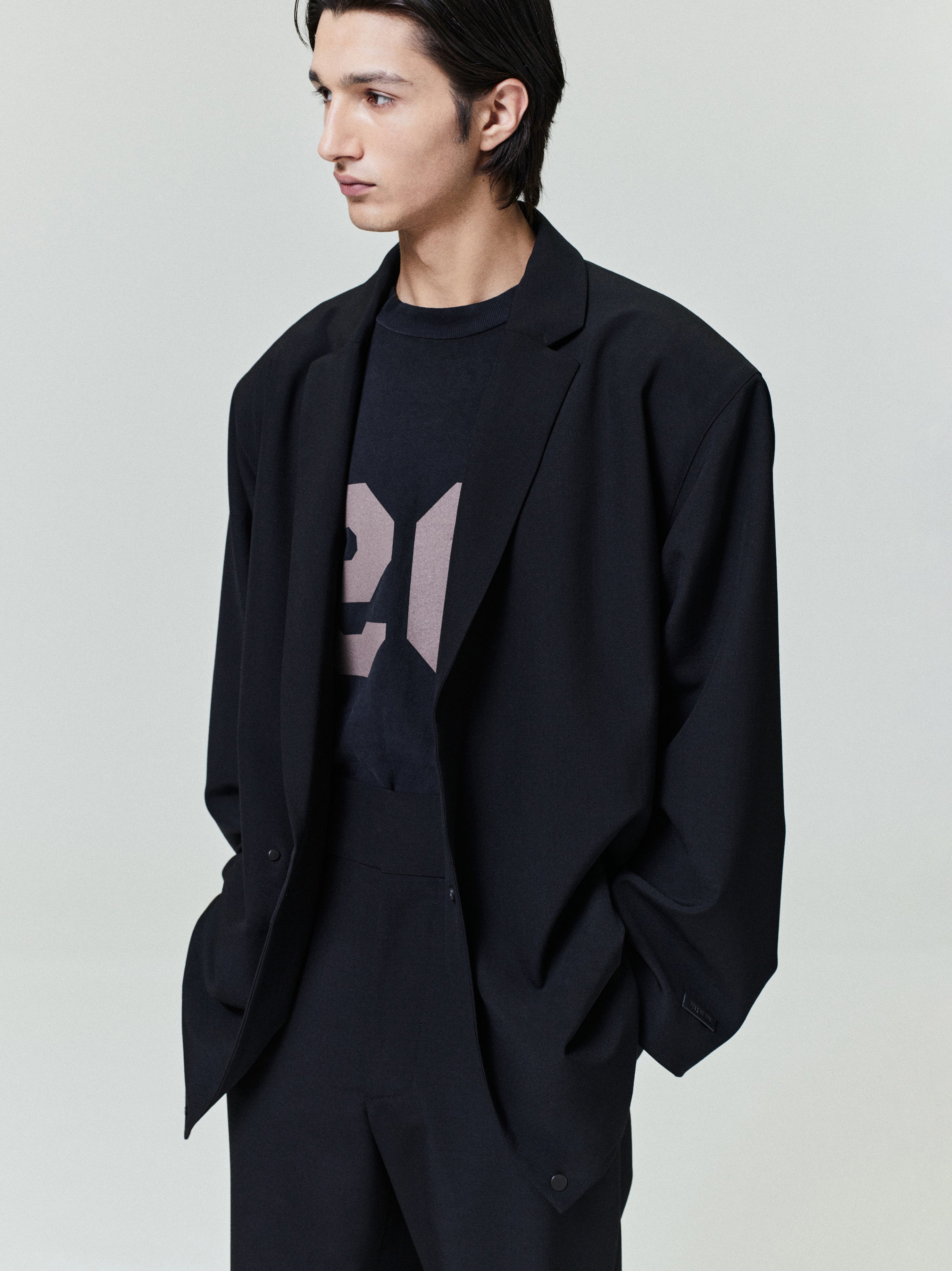 Young man wearing a loose black blazer over a graphic black t-shirt with matching black trousers, hands in pockets