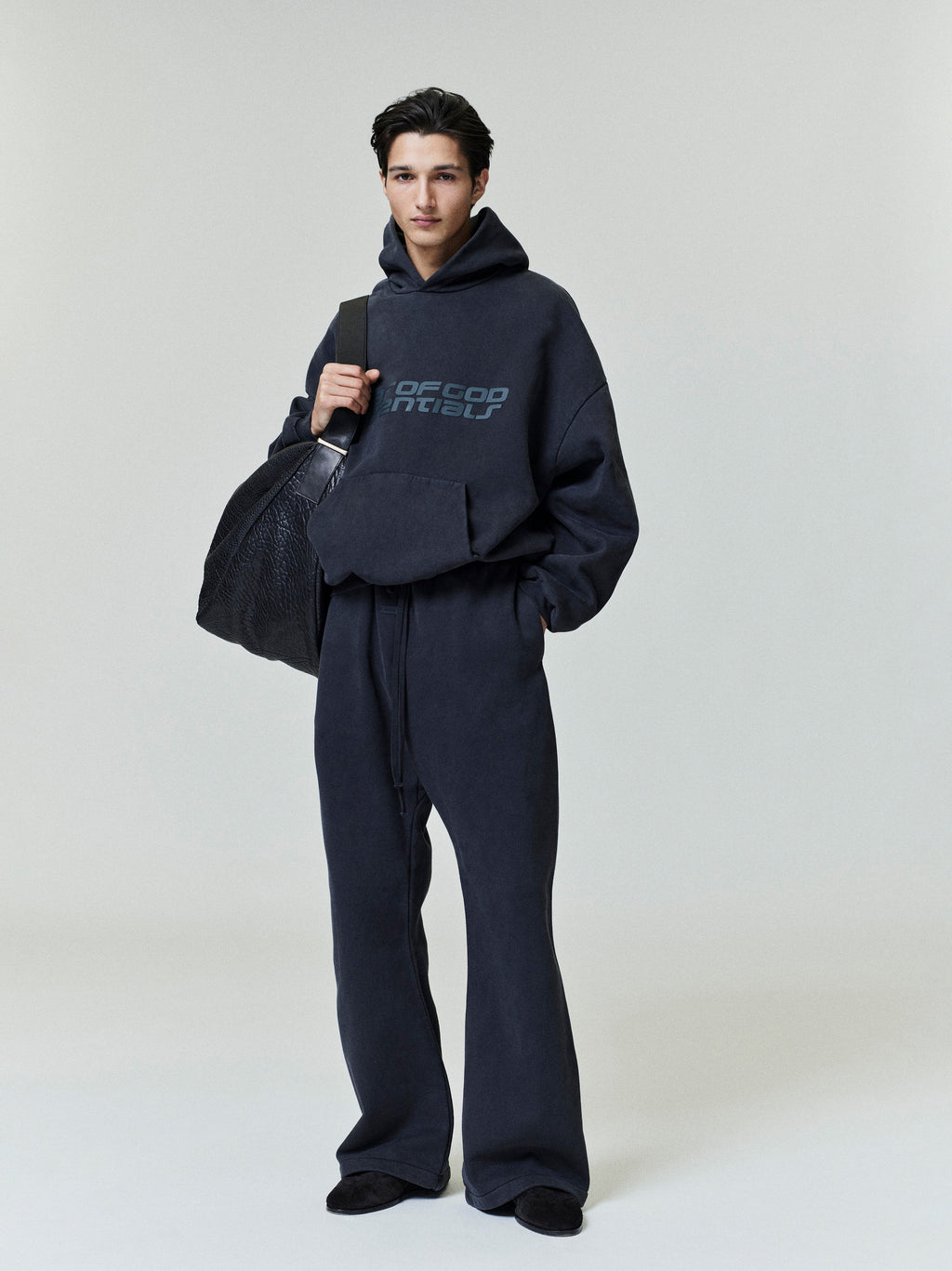 Model wearing dark navy Heavy Fleece 90s Hoodie with matching pants and carrying large black textured bag gallery 0