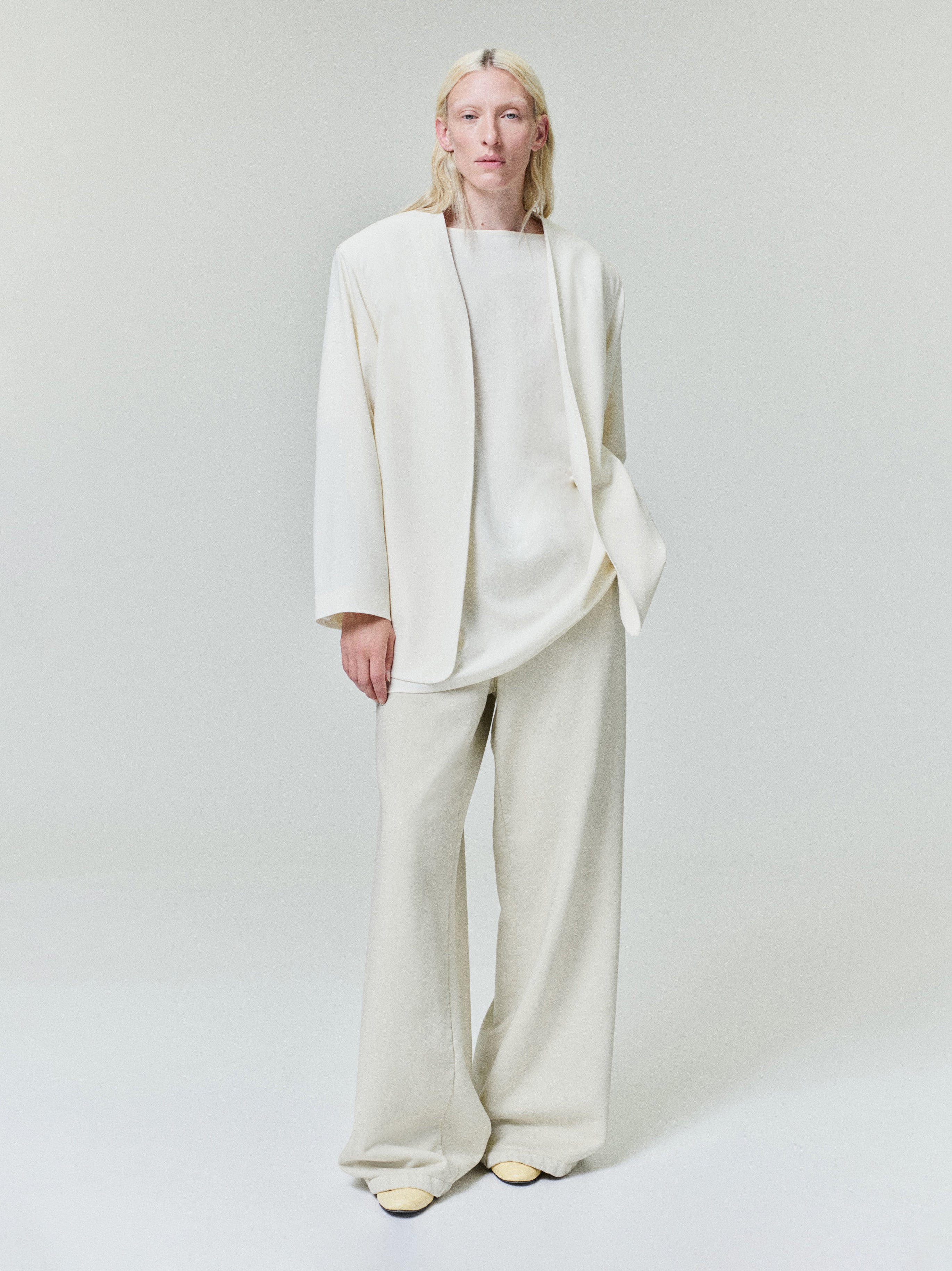 Model wearing an oversized cream jacket over a loose matching top and wide-leg pants on a neutral background