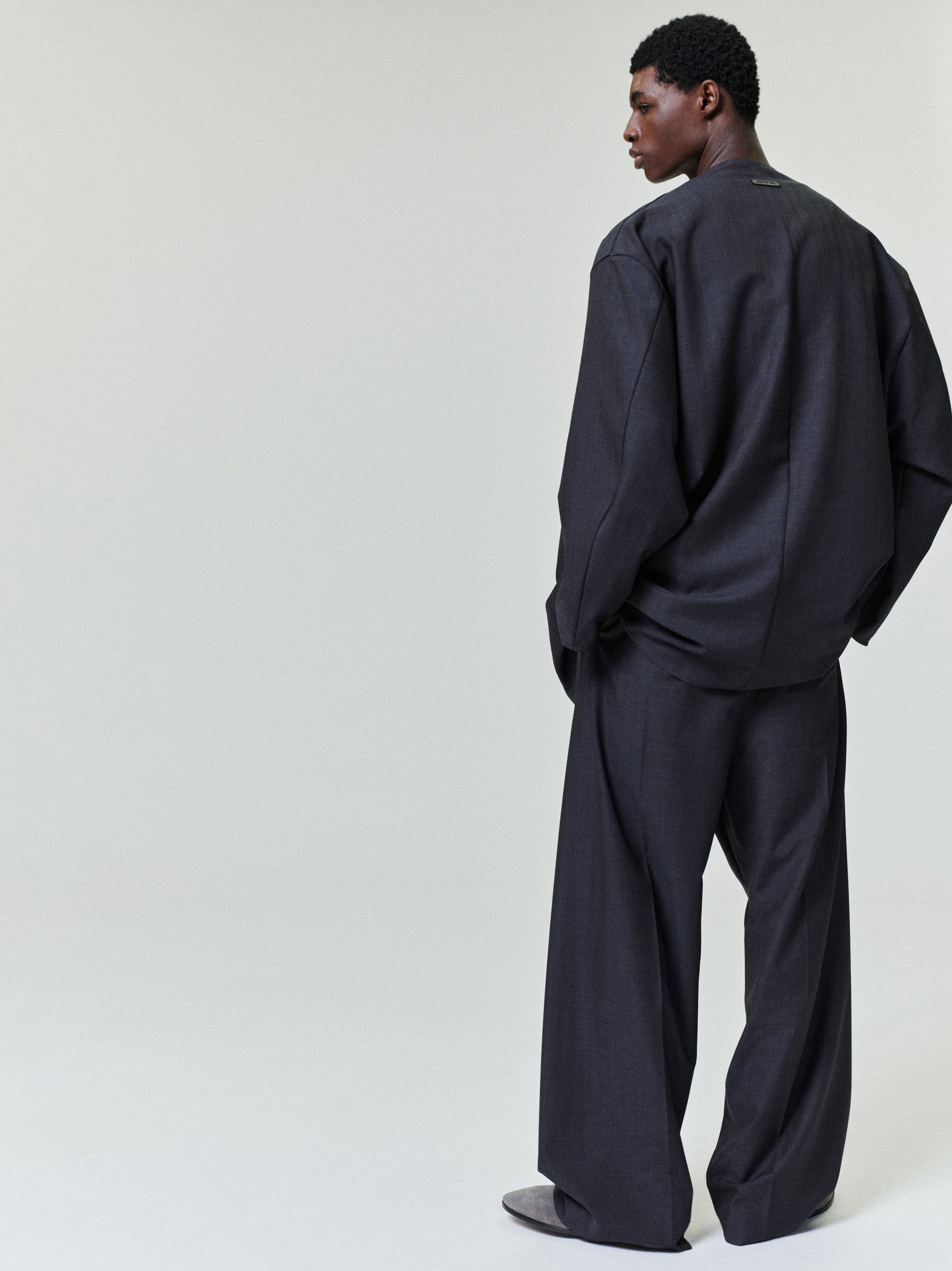 Male model seen from behind wearing loose dark gray oversized long-sleeve top and wide-leg matching trousers