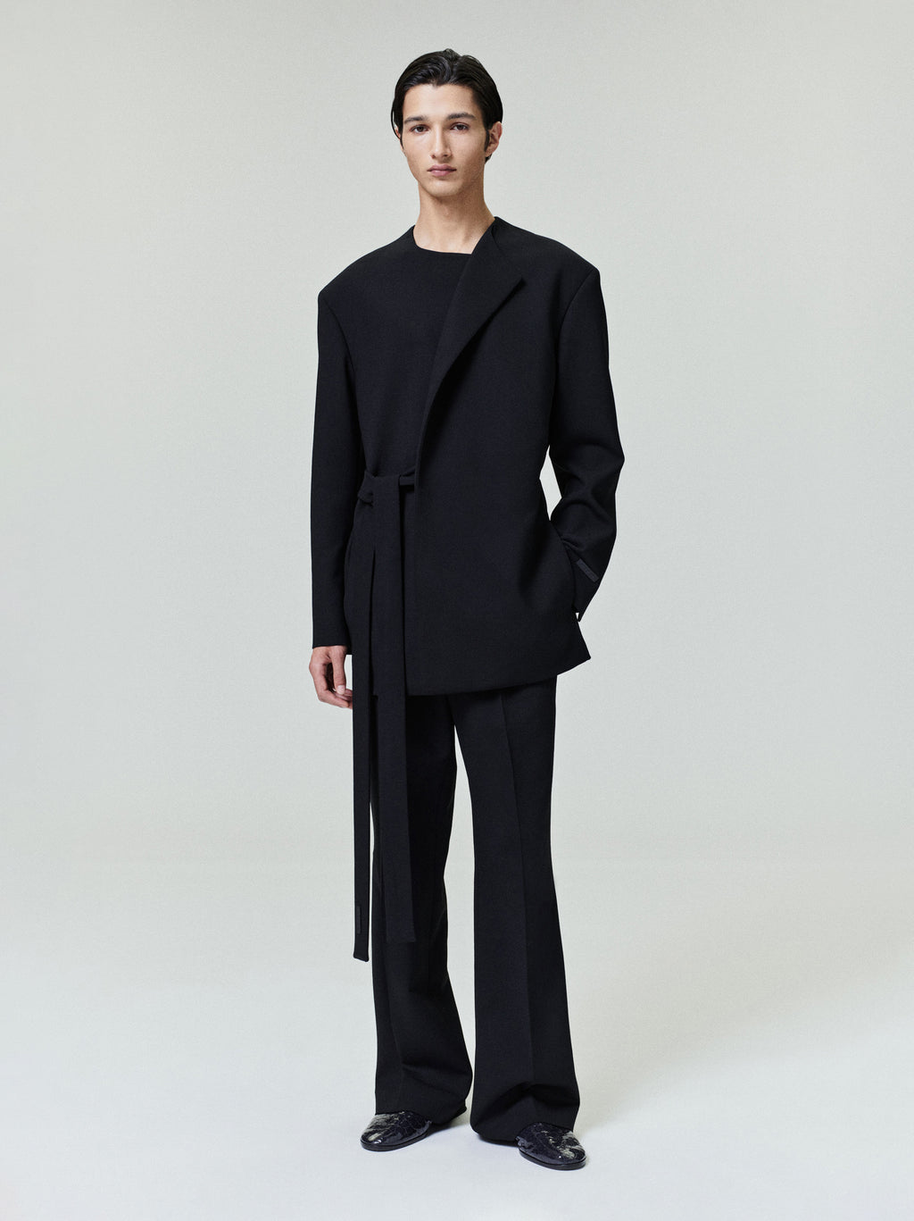 model wearing relaxed tailored black double weave wool crewneck jacket with long belt and matching wide-leg pants