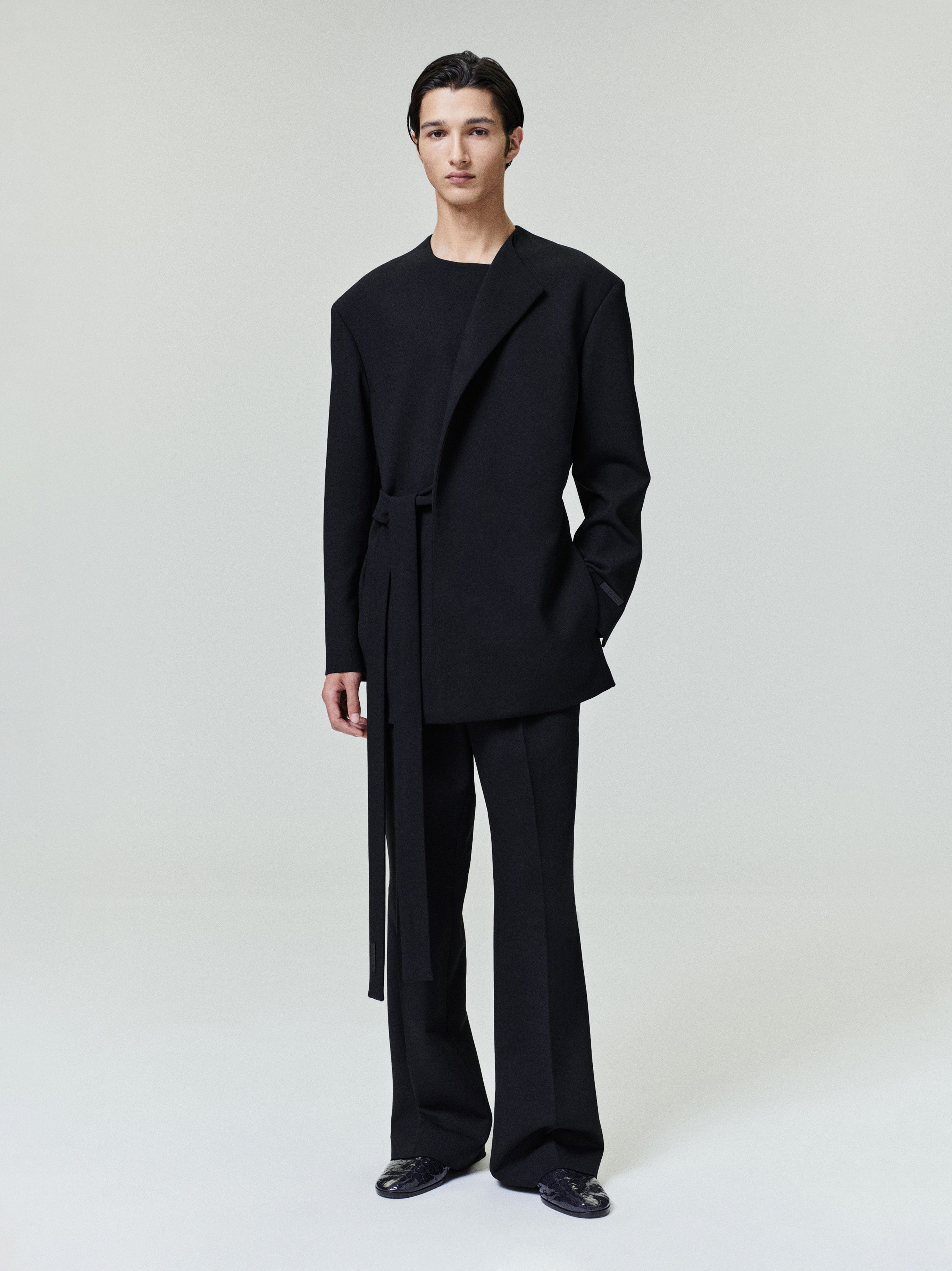 model wearing relaxed tailored black double weave wool crewneck jacket with long belt and matching wide-leg pants