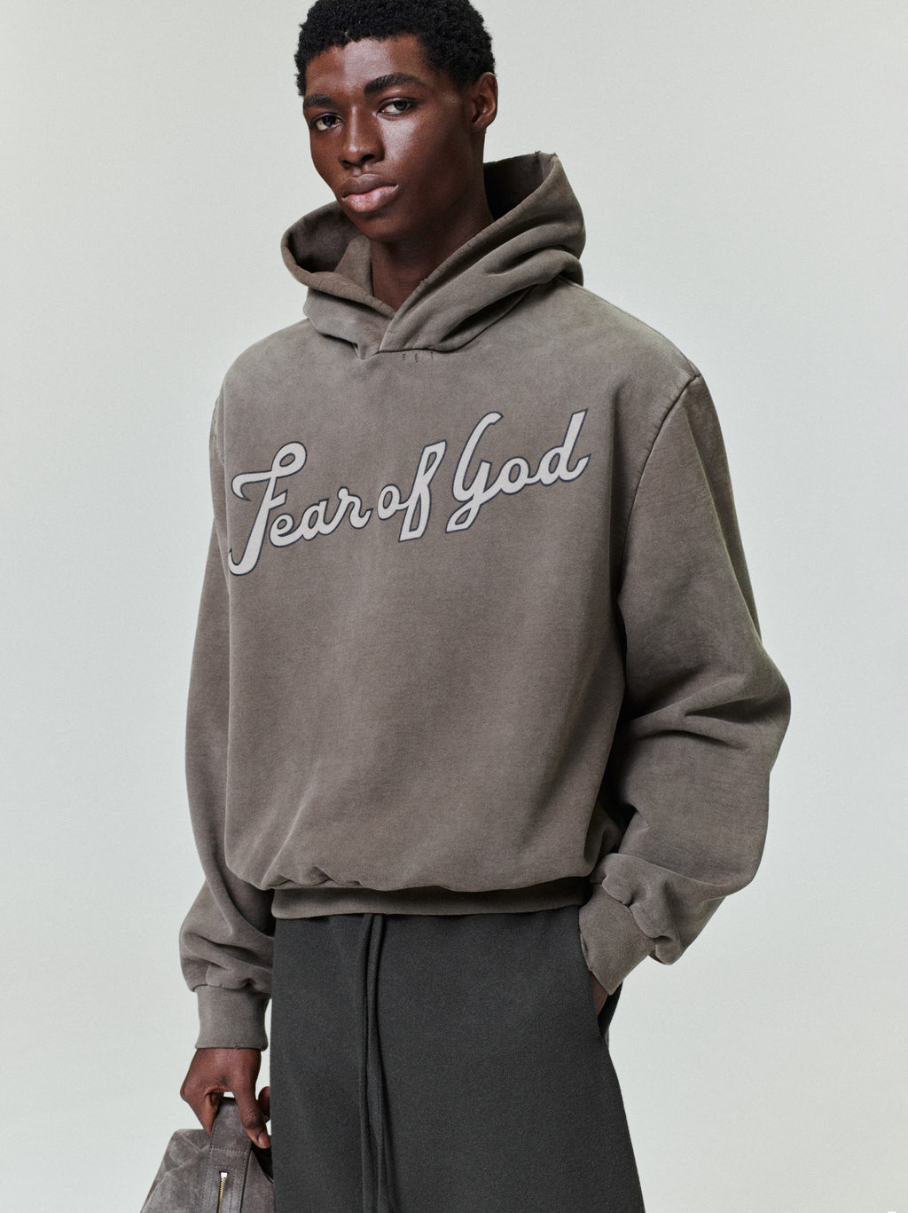 male model wearing sun-faded heavyweight cotton fleece hoodie with hand-printed "Fear of God" script across chest