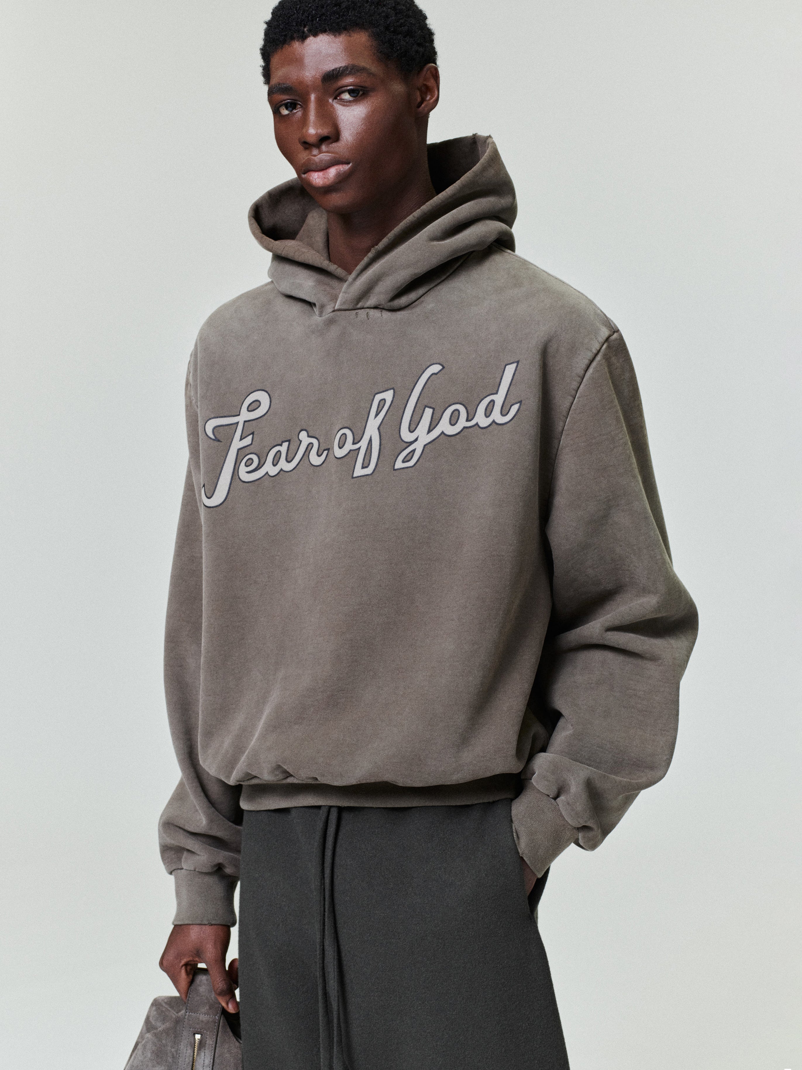 male model wearing sun-faded heavyweight cotton fleece hoodie with hand-printed "Fear of God" script across chest