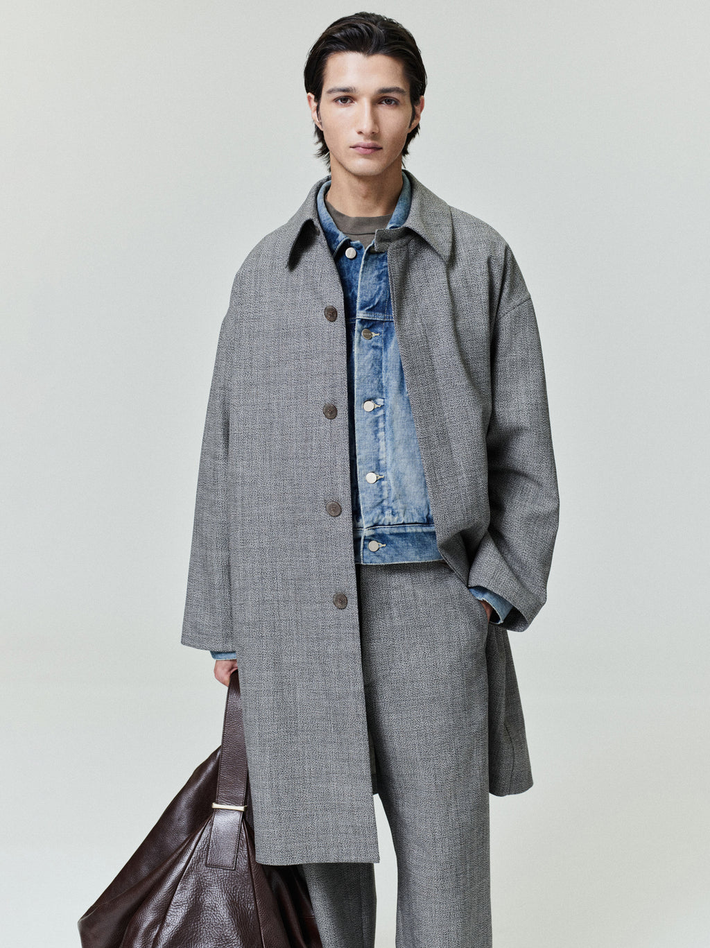model wearing gray mouline wool relaxed trench coat over blue denim jacket holding brown leather bag
