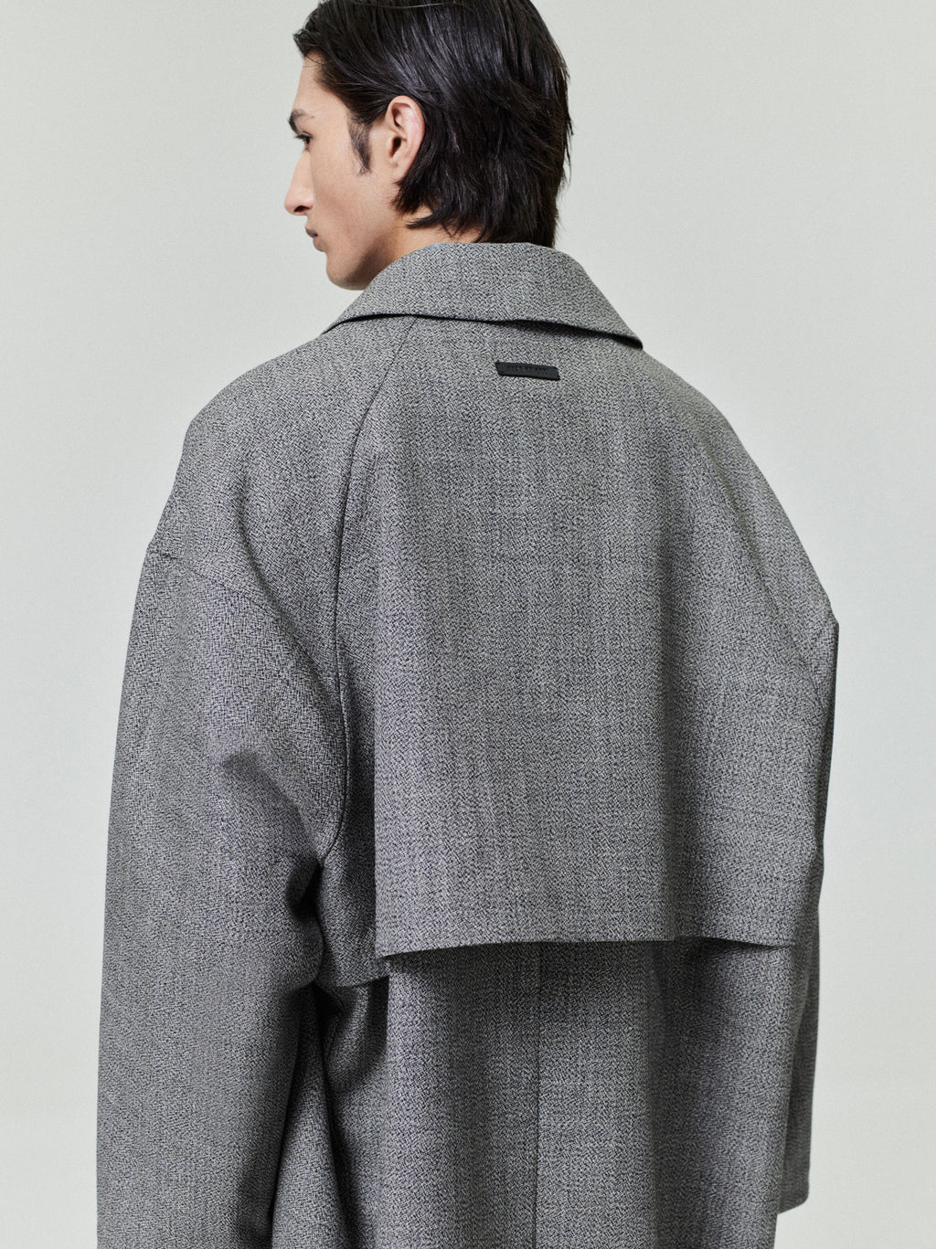 rear view of model wearing gray mouline wool relaxed trench coat with storm-flap back yoke and loose fit silhouette