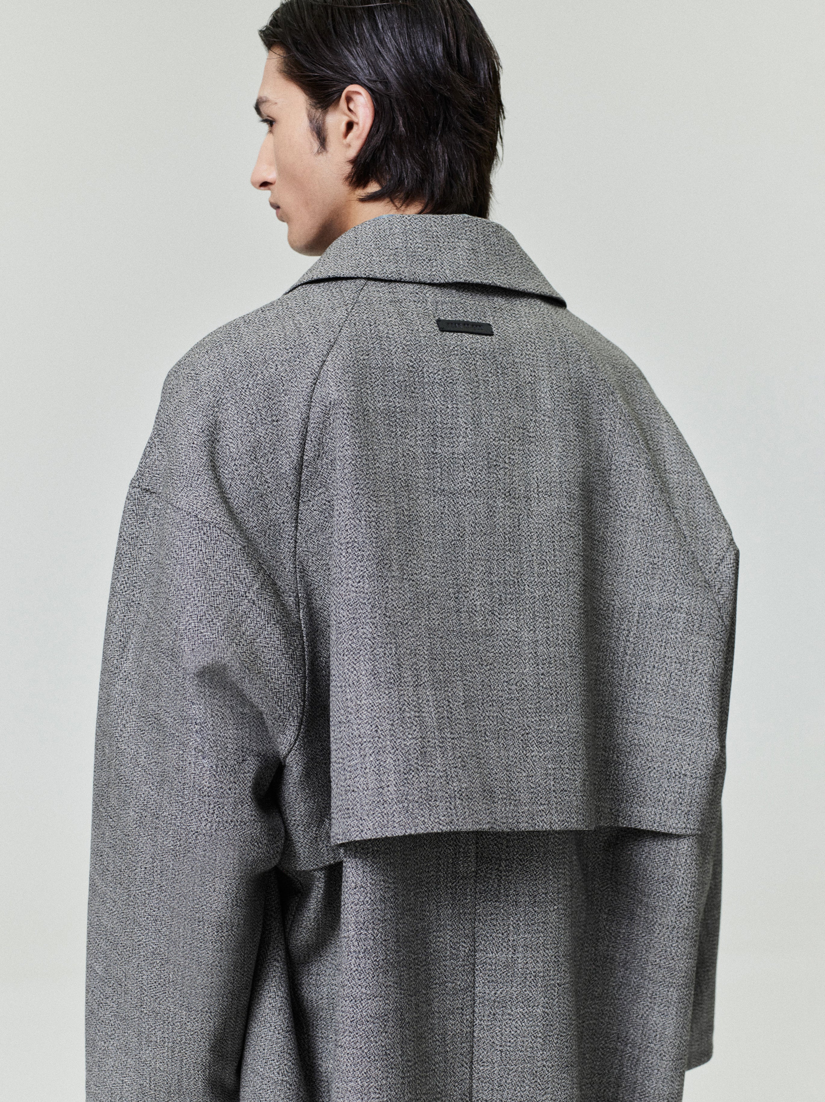rear view of model wearing gray mouline wool relaxed trench coat with storm-flap back yoke and loose fit silhouette