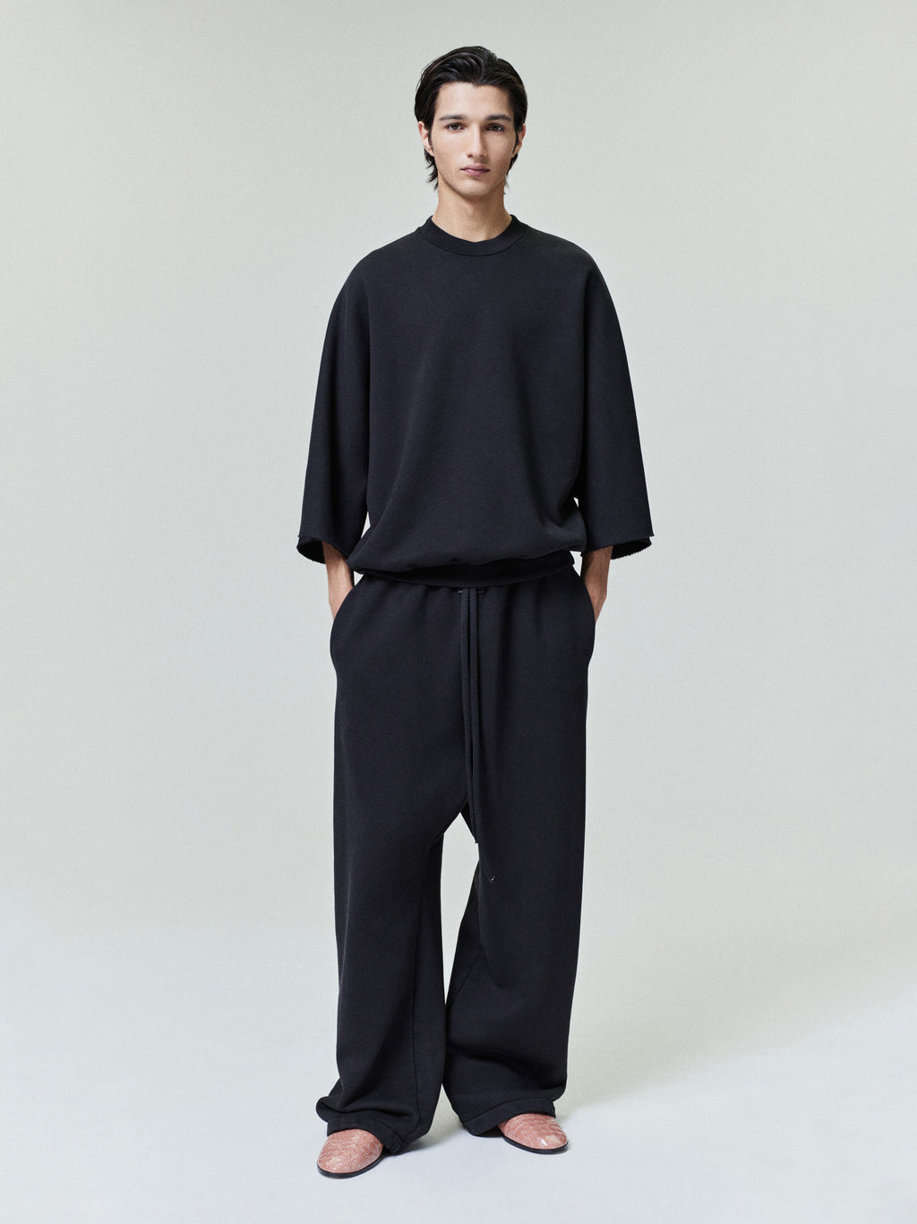 male model wearing black wide leg cotton fleece sweatpants with elastic drawstring waist and side pockets front view