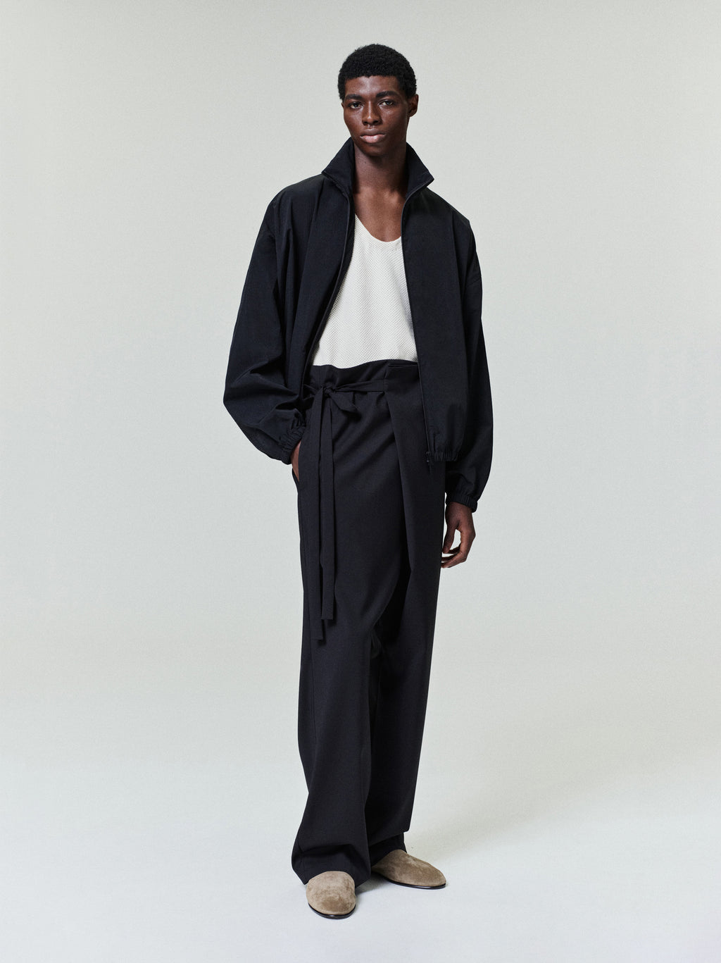 male model wearing relaxed black ripstop nylon track jacket with high collar and elasticated cuffs, paired with wide-leg trousers