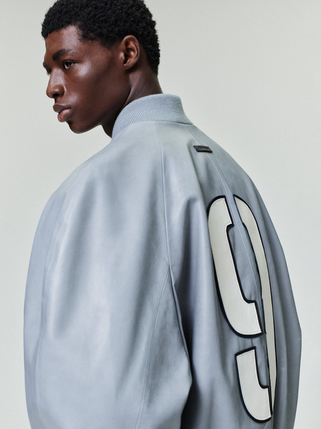 Side profile of a man wearing a light gray jacket with a large white number 9 on the back and a ribbed collar