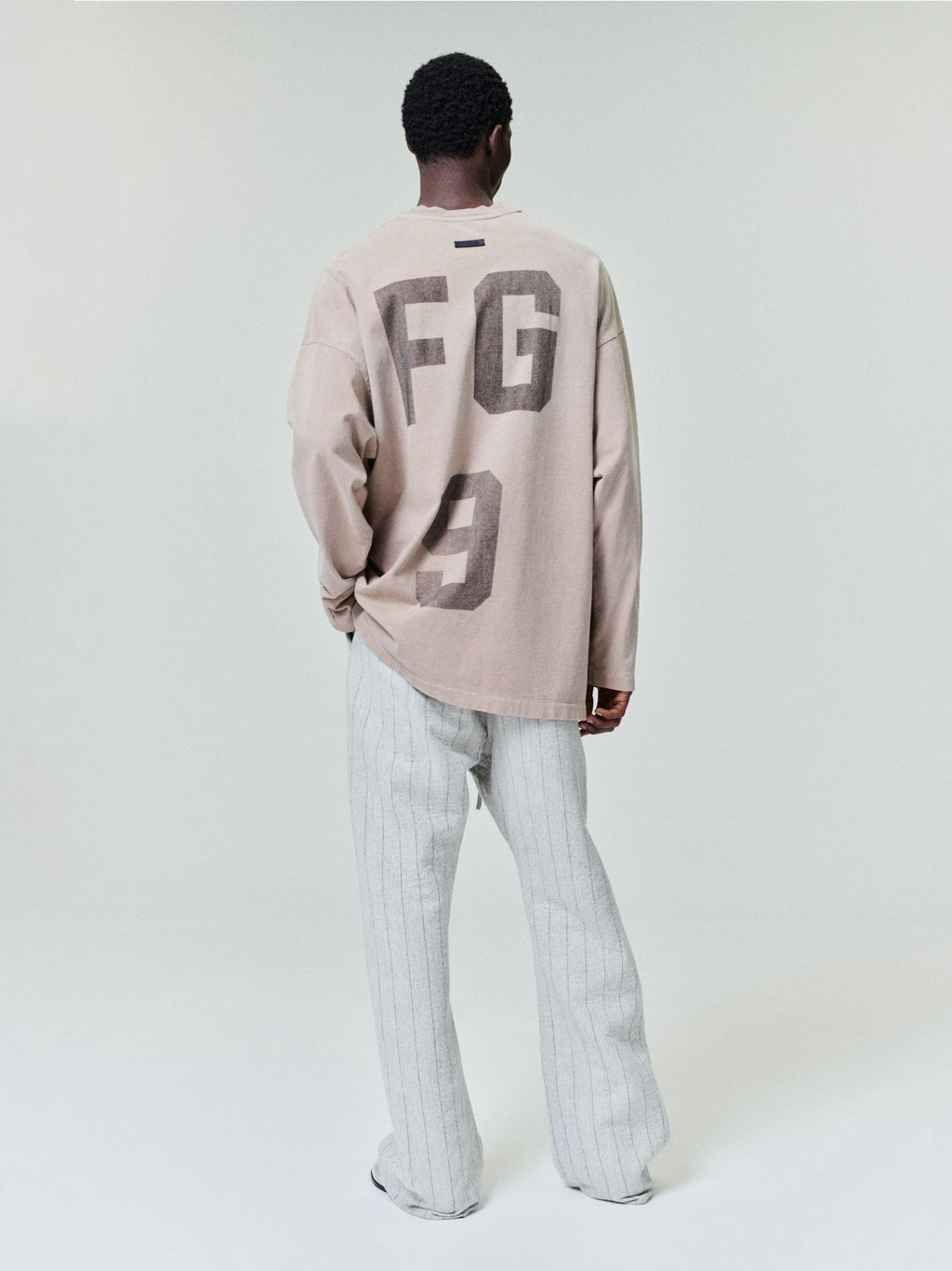 model wearing a faded beige heavyweight cotton jersey long sleeve tee with large “FG 9” graphic on back