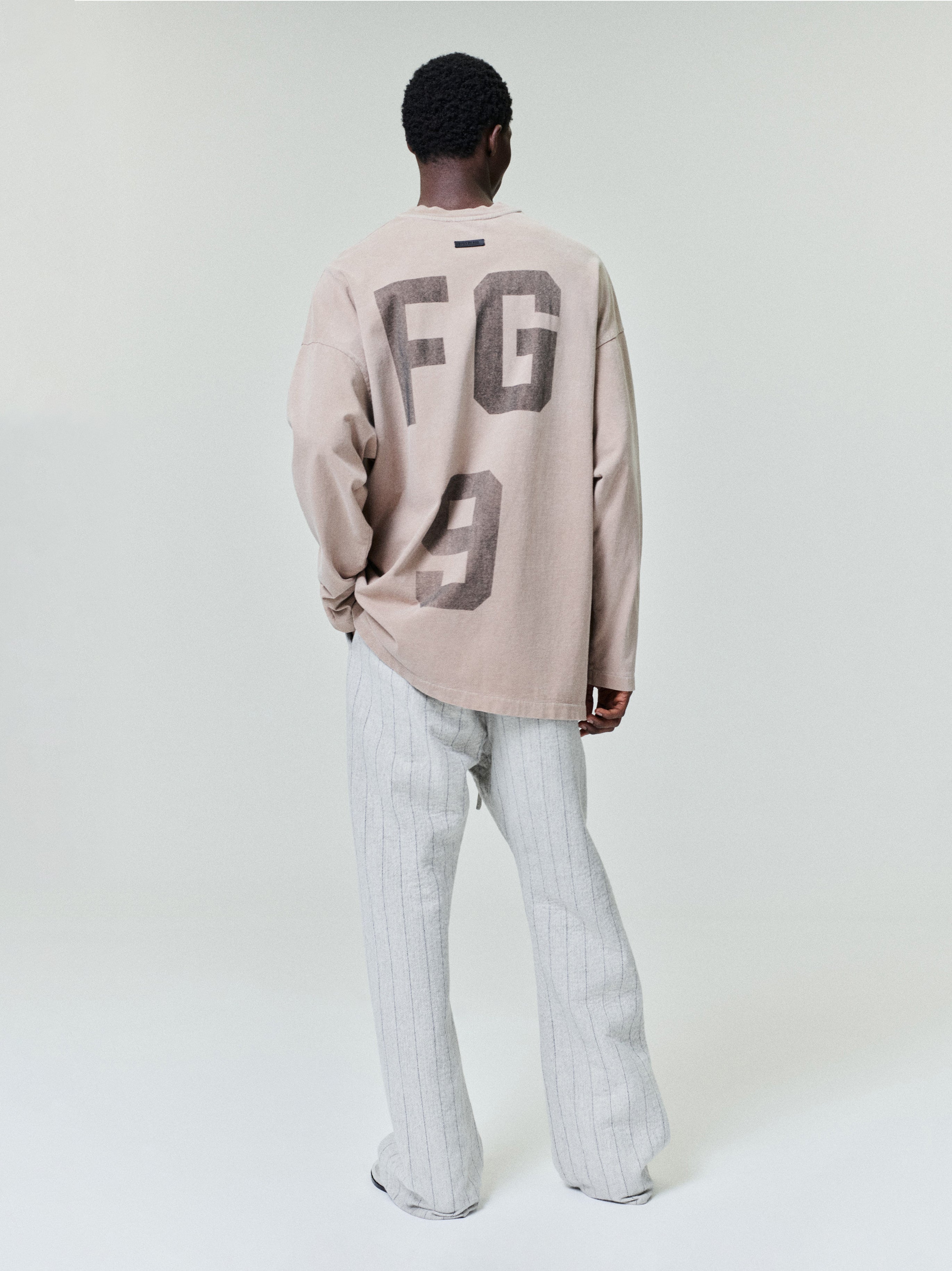 model wearing a faded beige heavyweight cotton jersey long sleeve tee with large “FG 9” graphic on back