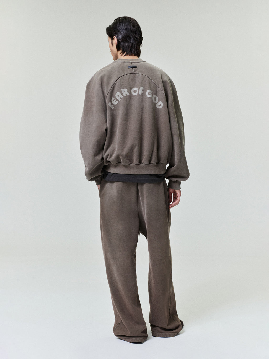 model wearing sunfaded dark brown wide leg sweatpants and matching sweatshirt with Fear of God logo on back