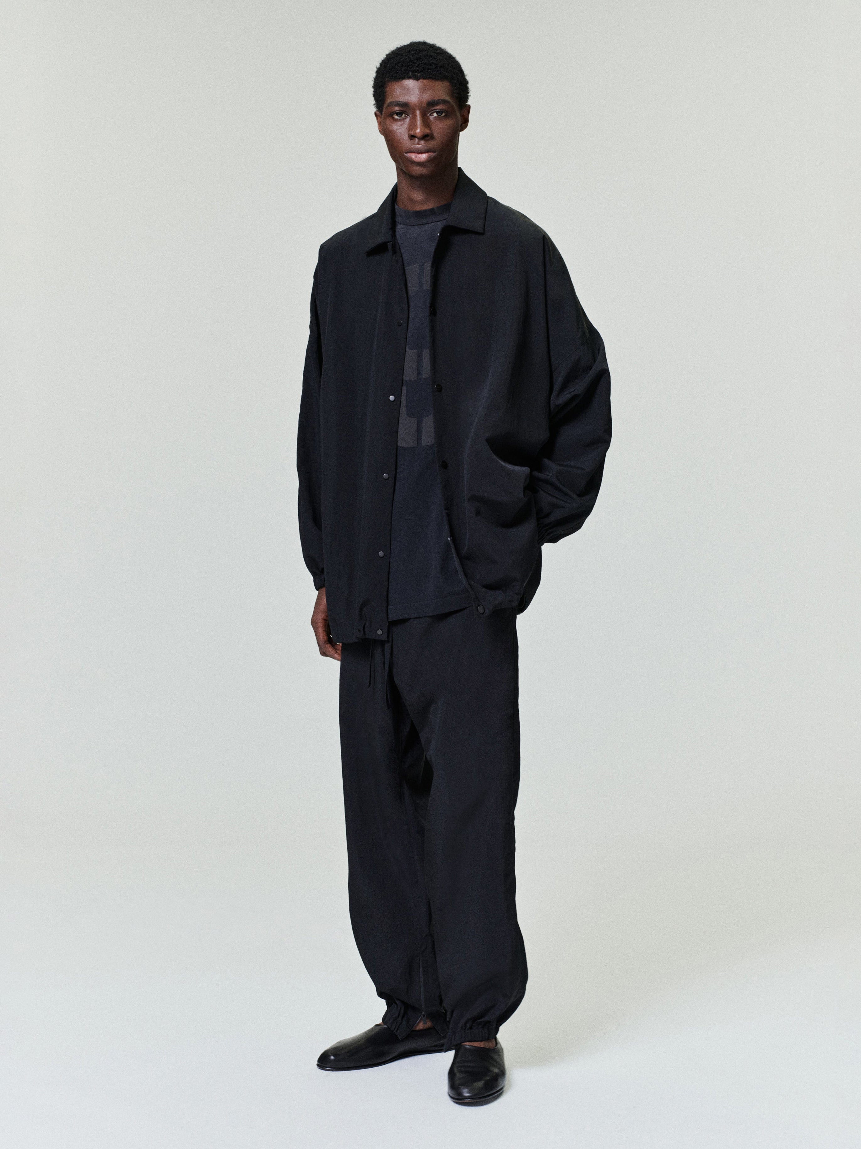 male model wearing black relaxed fit nylon ripstop tech track pants with elastic cuffs and matching oversized jacket