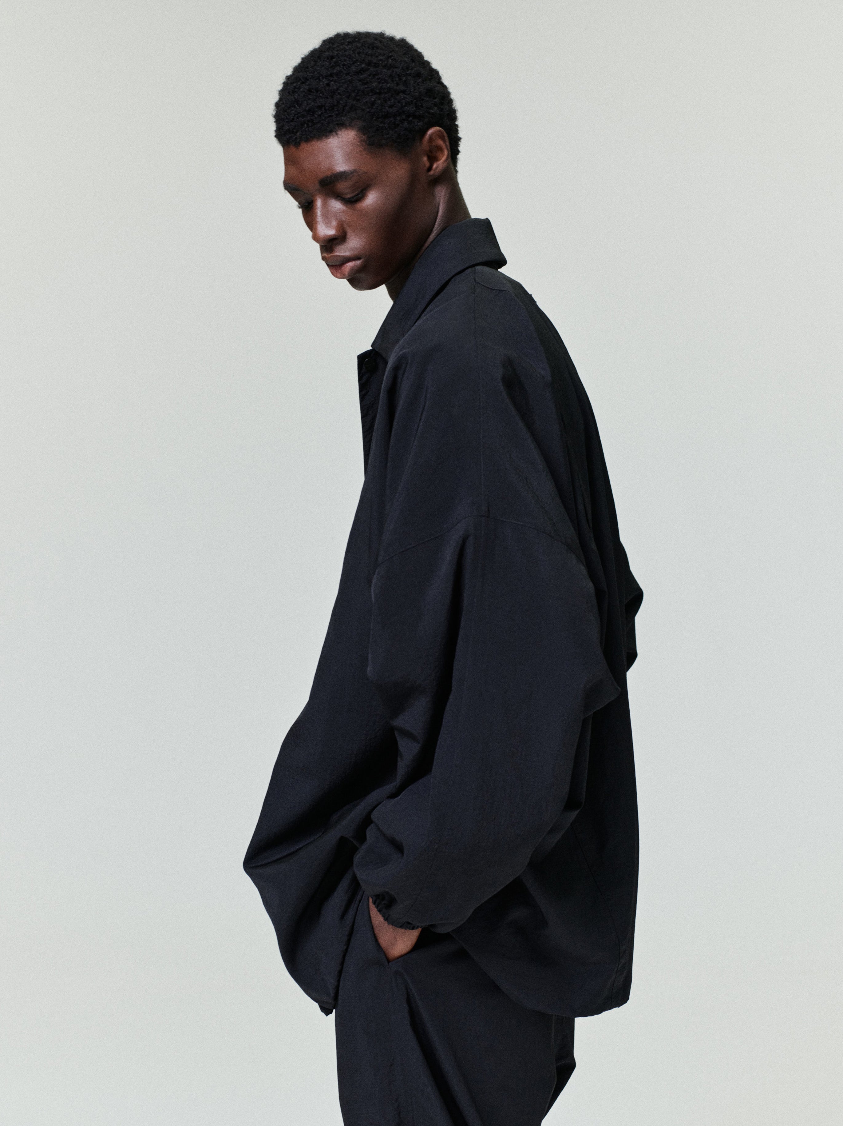 side view of man wearing black oversized lightweight recycled nylon ripstop tech windbreaker jacket