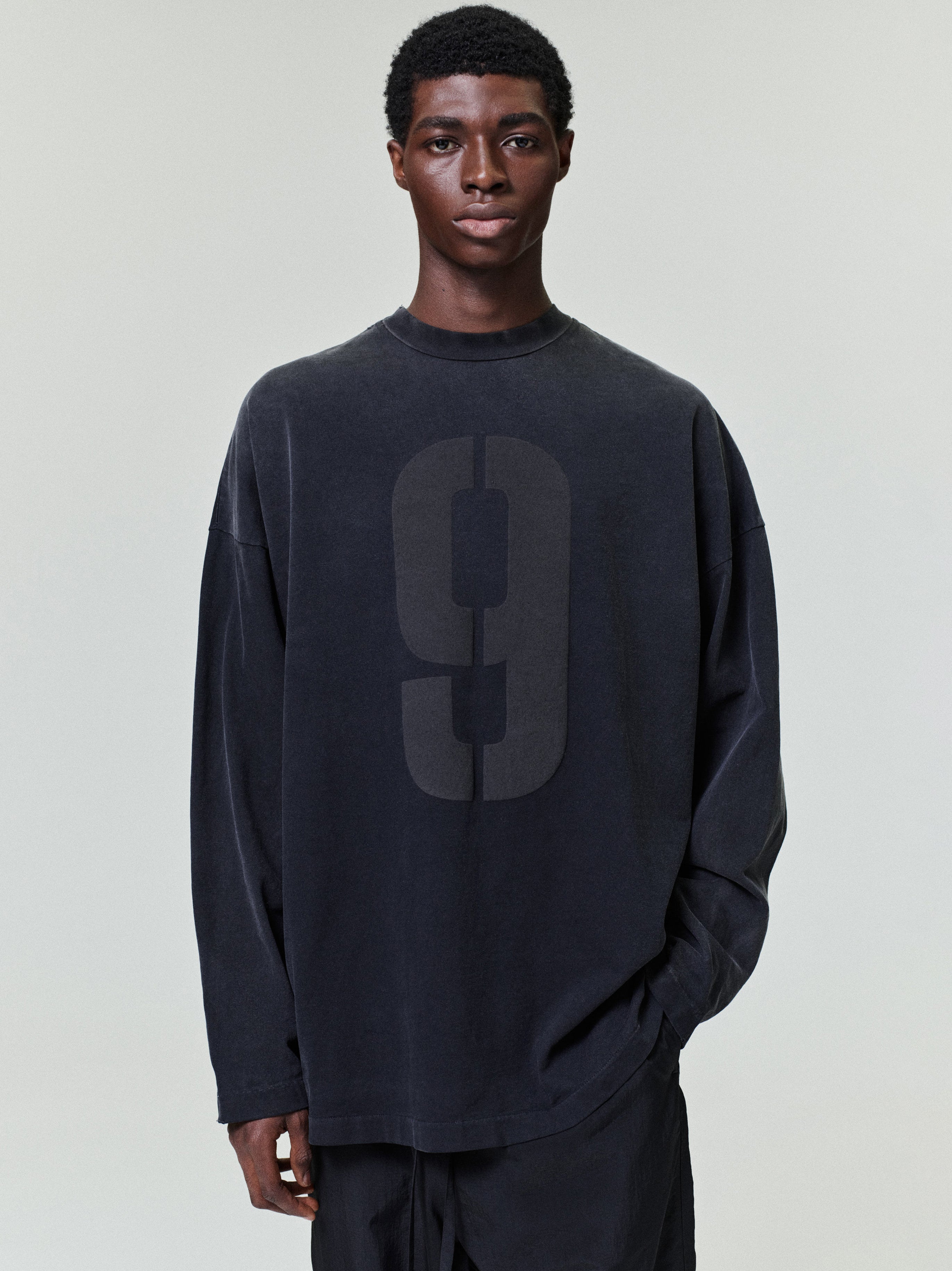 model wearing a faded black heavyweight cotton long sleeve tee with large subtle number 9 printed on front