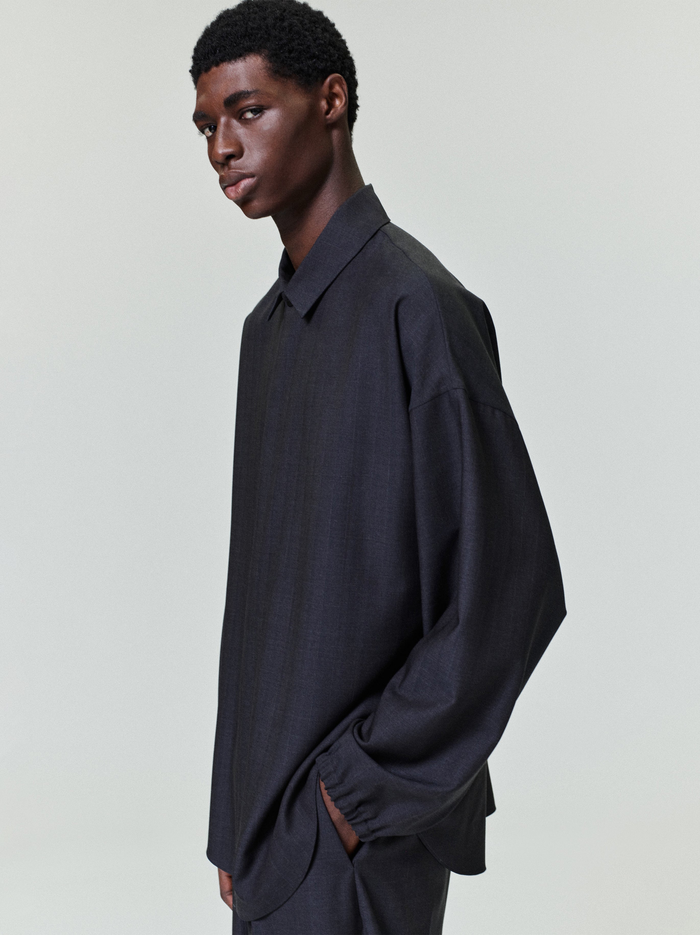 Young man wearing a loose-fitting dark charcoal long-sleeve shirt with a classic collar standing sideways