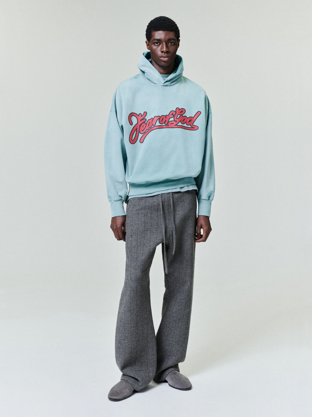 Full-length view of a model wearing a light blue hoodie with red script text and gray wide-leg pants against a plain background
