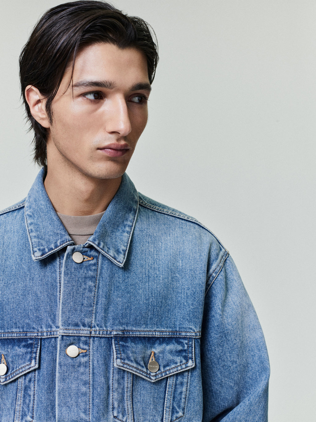 Young man wearing a classic medium-blue denim jacket with flap chest pockets and metal button closures