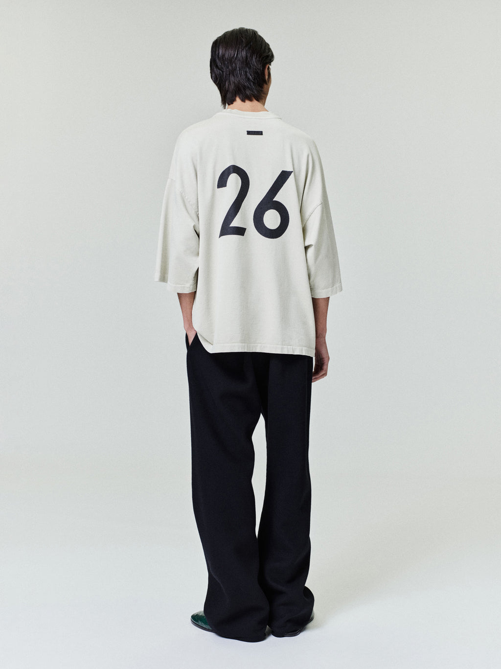 Rear view of a man wearing an oversized light beige shirt with large black number 26 and wide black pants