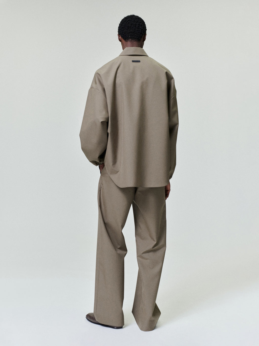 Man wearing a loose taupe long-sleeve shirt with matching wide-leg trousers standing against a plain background