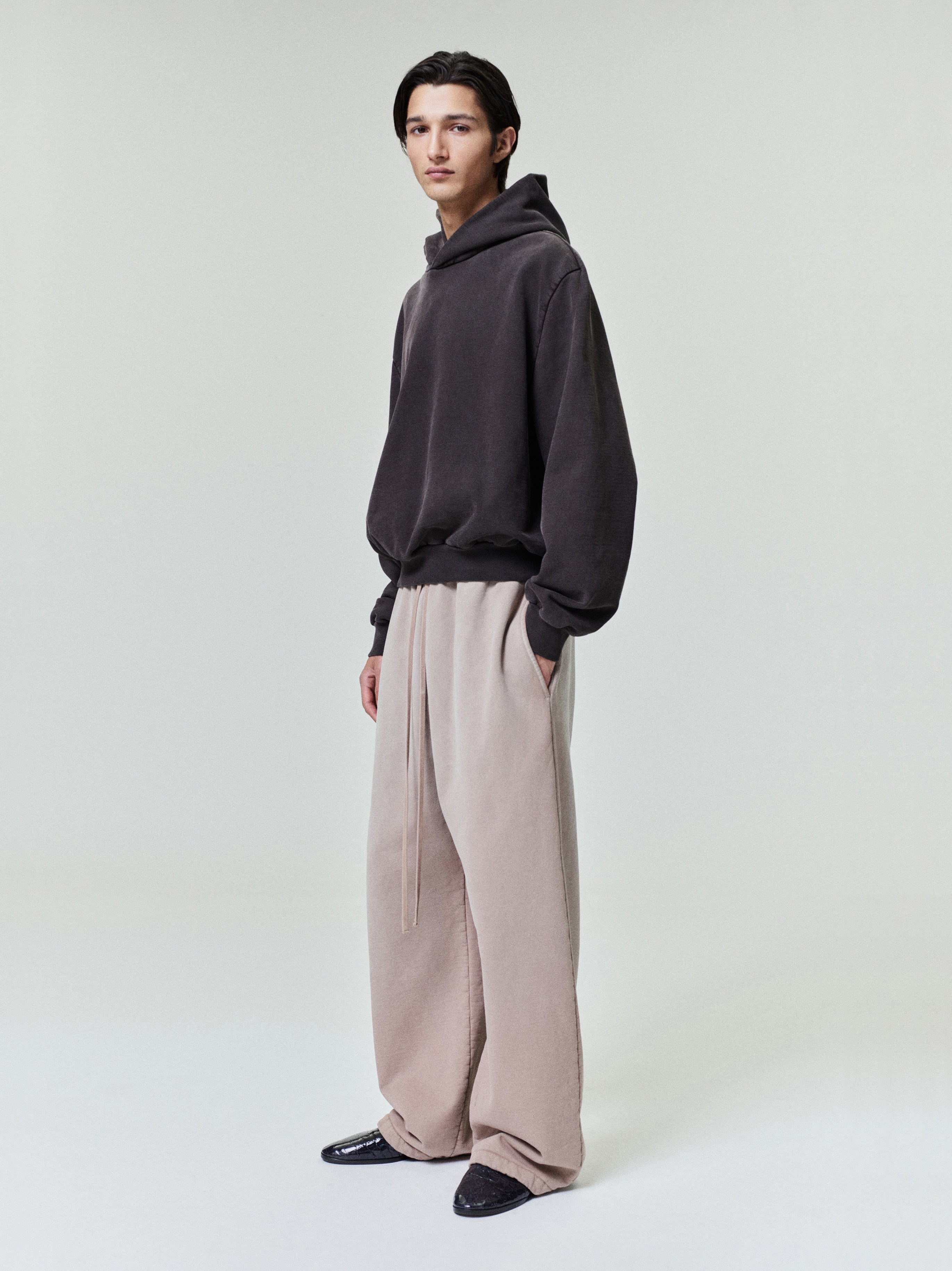 male model wearing light beige wide leg sweatpants with relaxed fit and dark hoodie in minimal studio setting