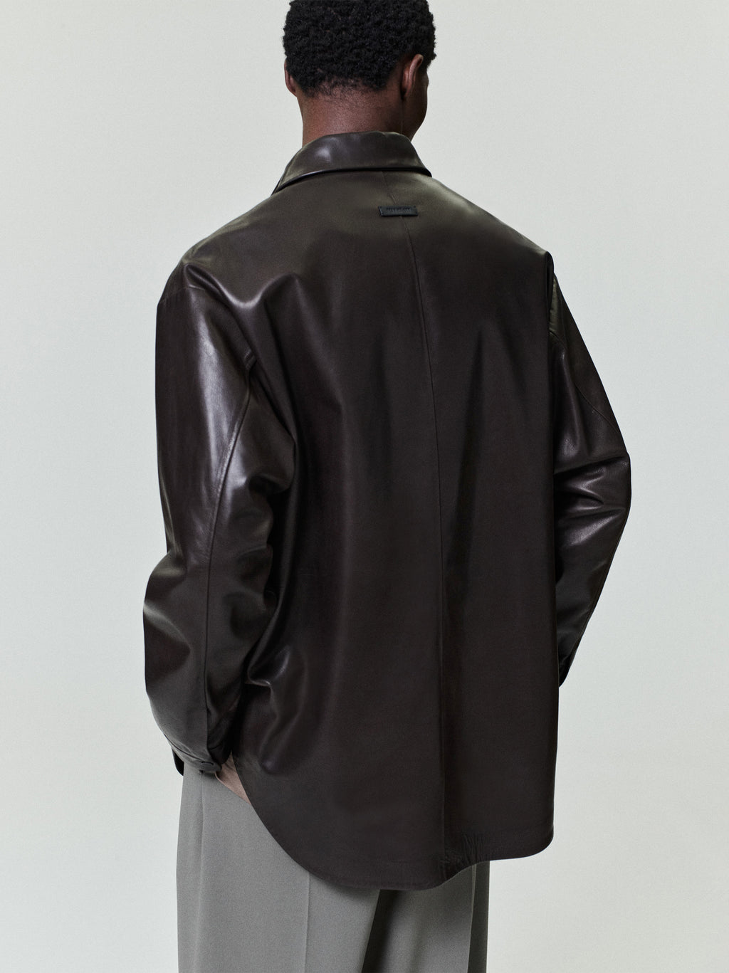 Man wearing an oversized dark brown leather shirt jacket with relaxed fit sleeves and light gray wide-leg trousers