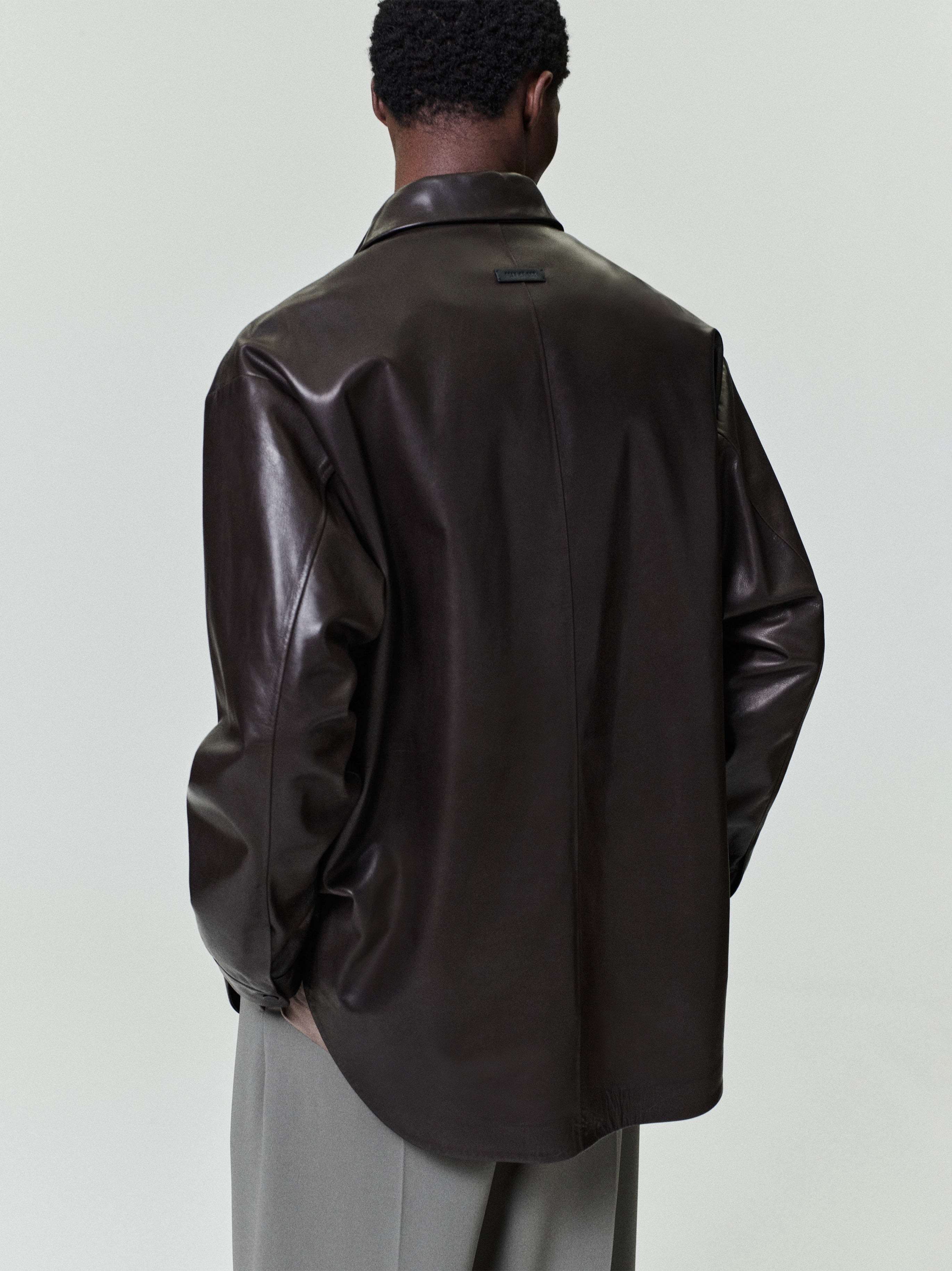 Man wearing an oversized dark brown leather shirt jacket with relaxed fit sleeves and light gray wide-leg trousers