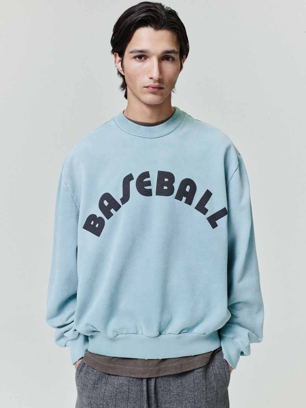 male model wearing sun-faded light blue heavyweight cotton fleece sweatshirt with bold black "BASEBALL" text on front