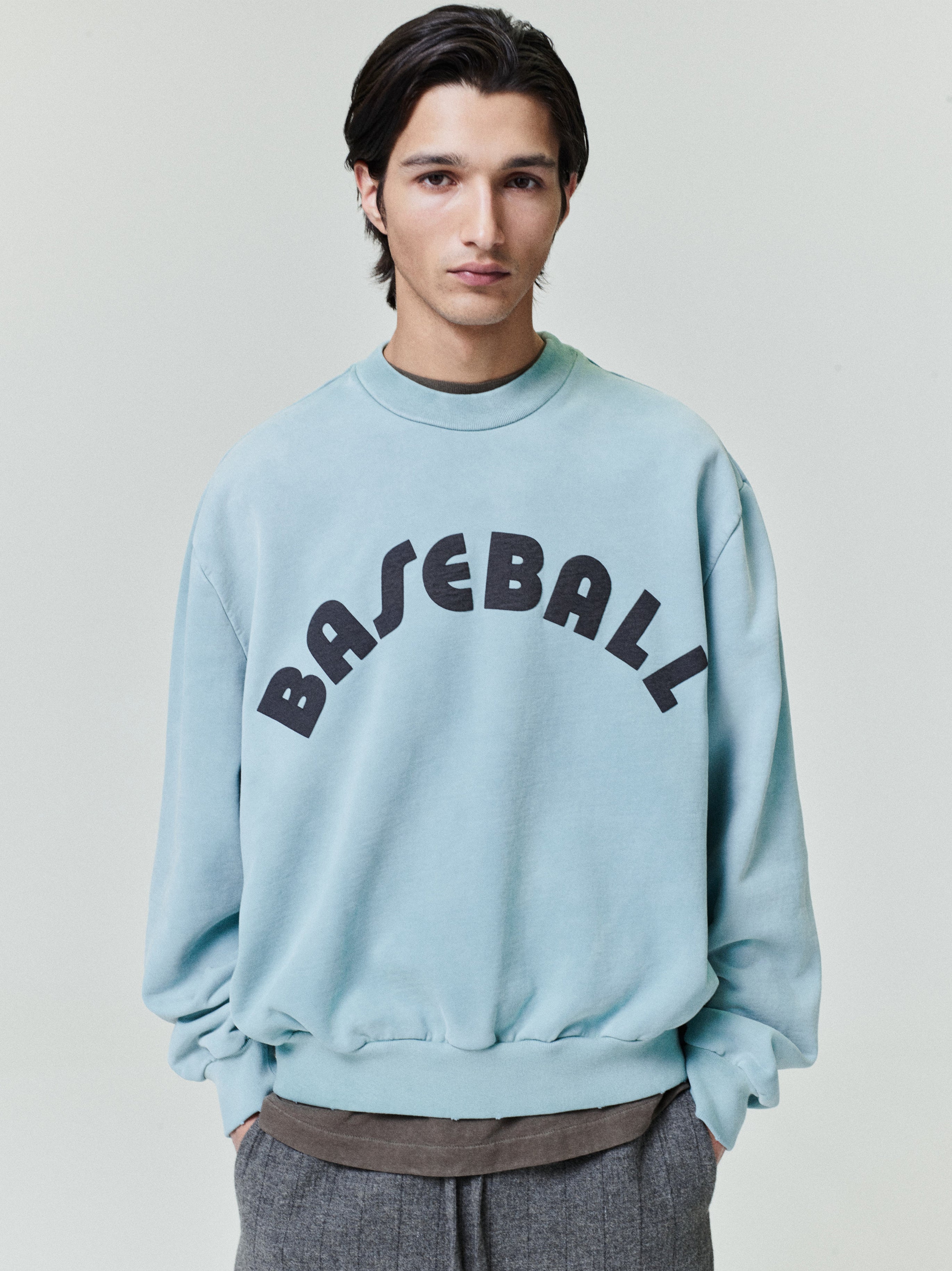 male model wearing sun-faded light blue heavyweight cotton fleece sweatshirt with bold black "BASEBALL" text on front