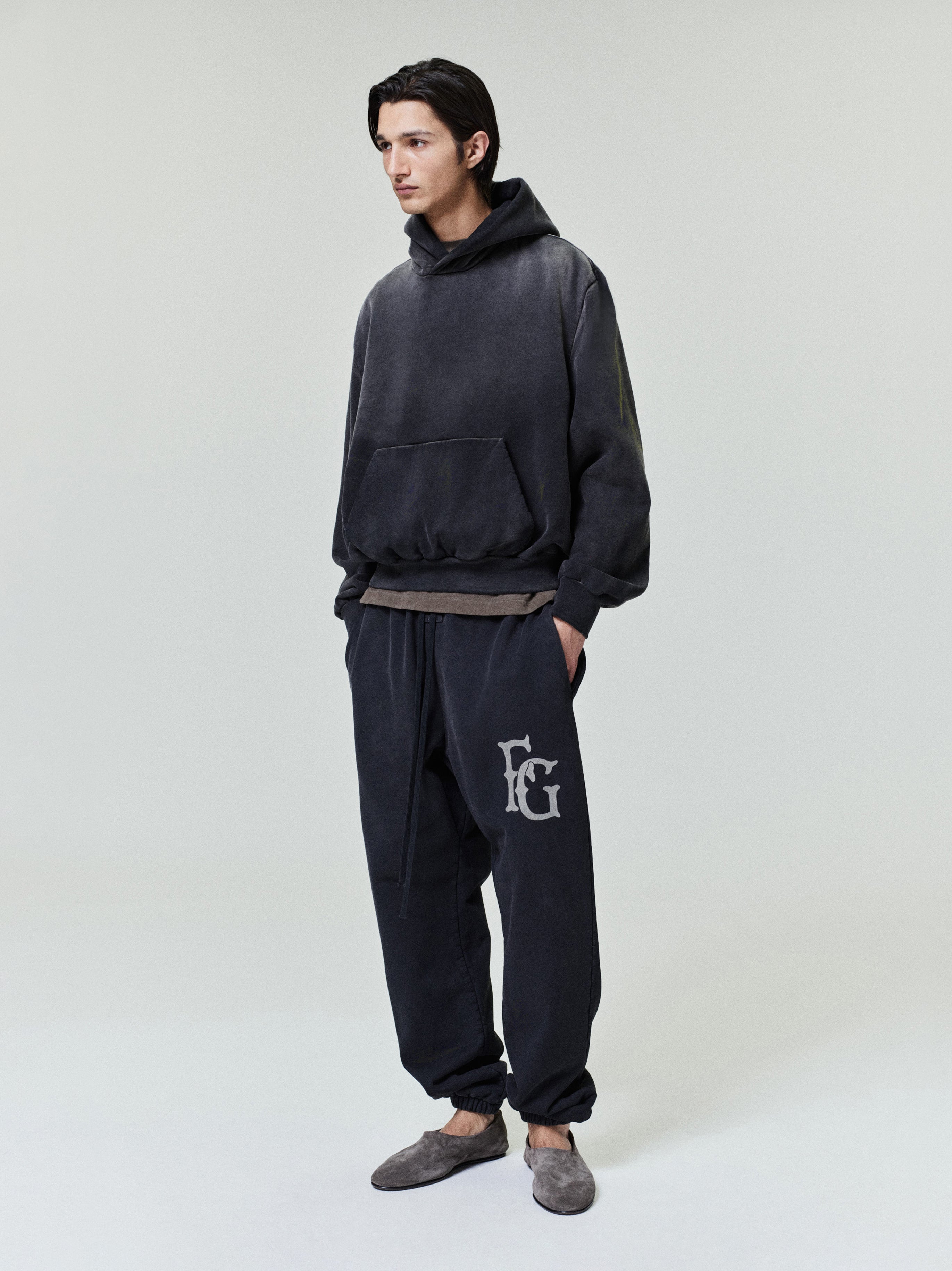 male model wearing washed black heavyweight cotton fleece sweatpants with FG logo on leg and elastic cuffs