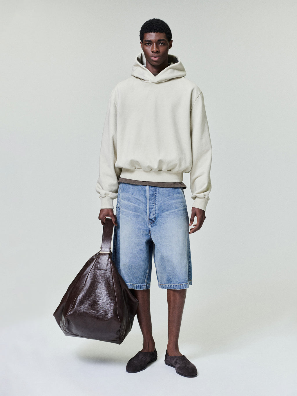 model wearing light blue denim utility shorts with relaxed fit and side pockets holding large brown leather bag