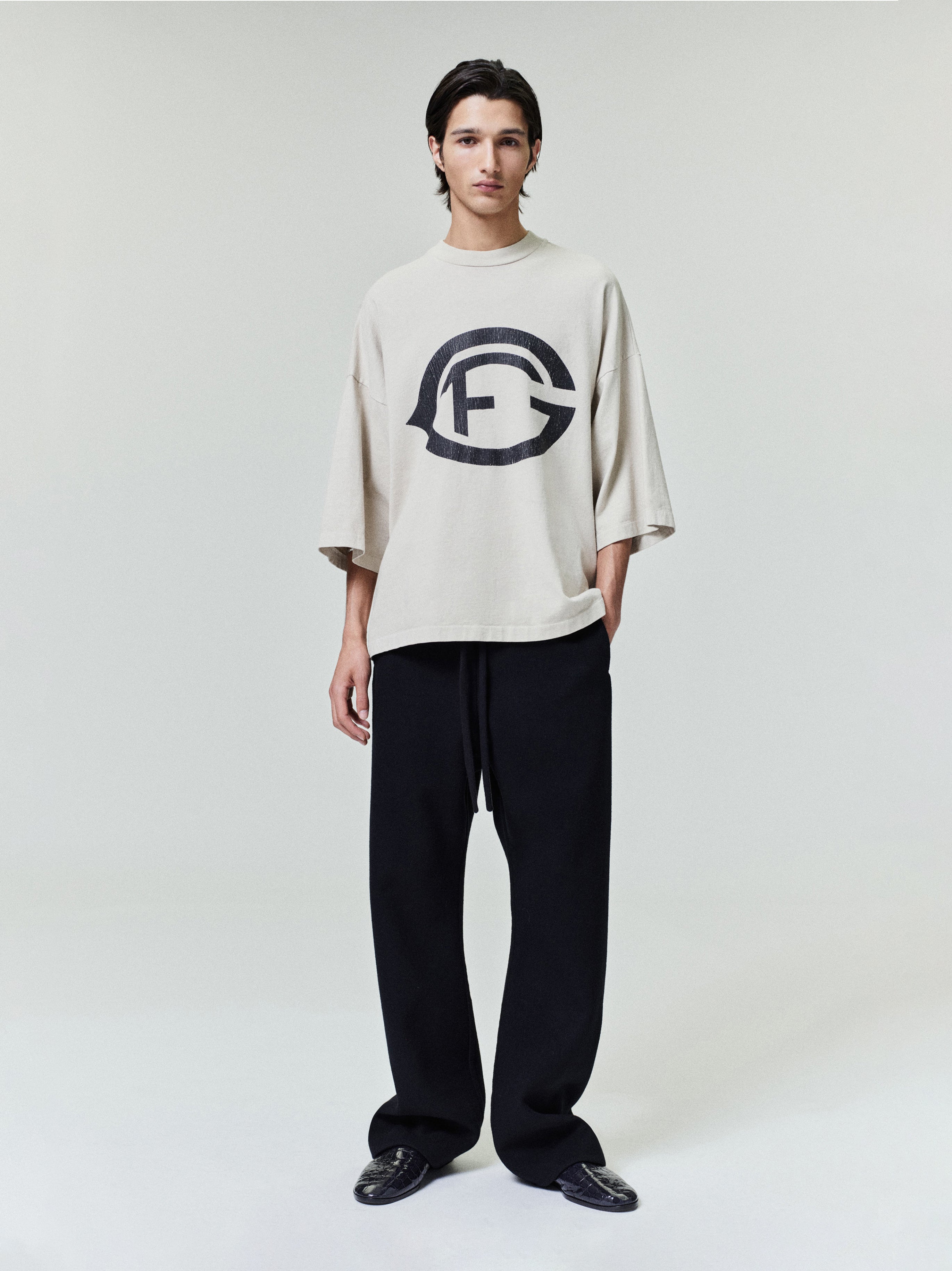 model wearing oversized sun-faded beige heavyweight cotton tee with large black FG emblem printed on front chest