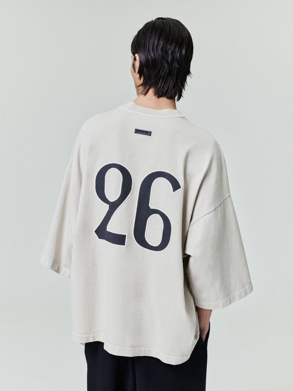 model wearing oversized light beige heavyweight cotton tee with large bold black number 26 printed on back