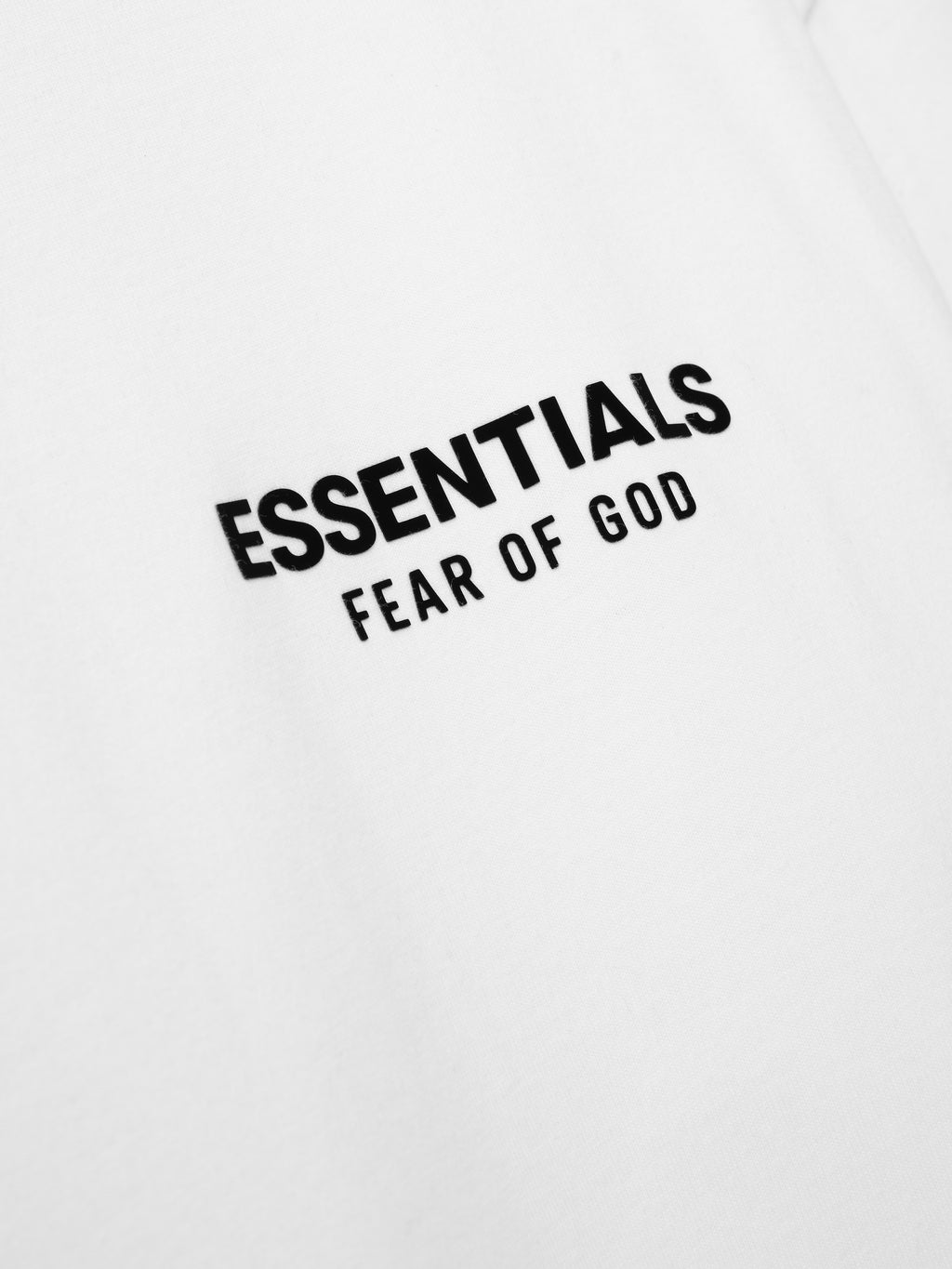Essentials SS26 Classic Long Sleeve Tee in bright white featuring bold black "ESSENTIALS FEAR OF GOD" text detail on the chest, showcasing minimalist streetwear style.